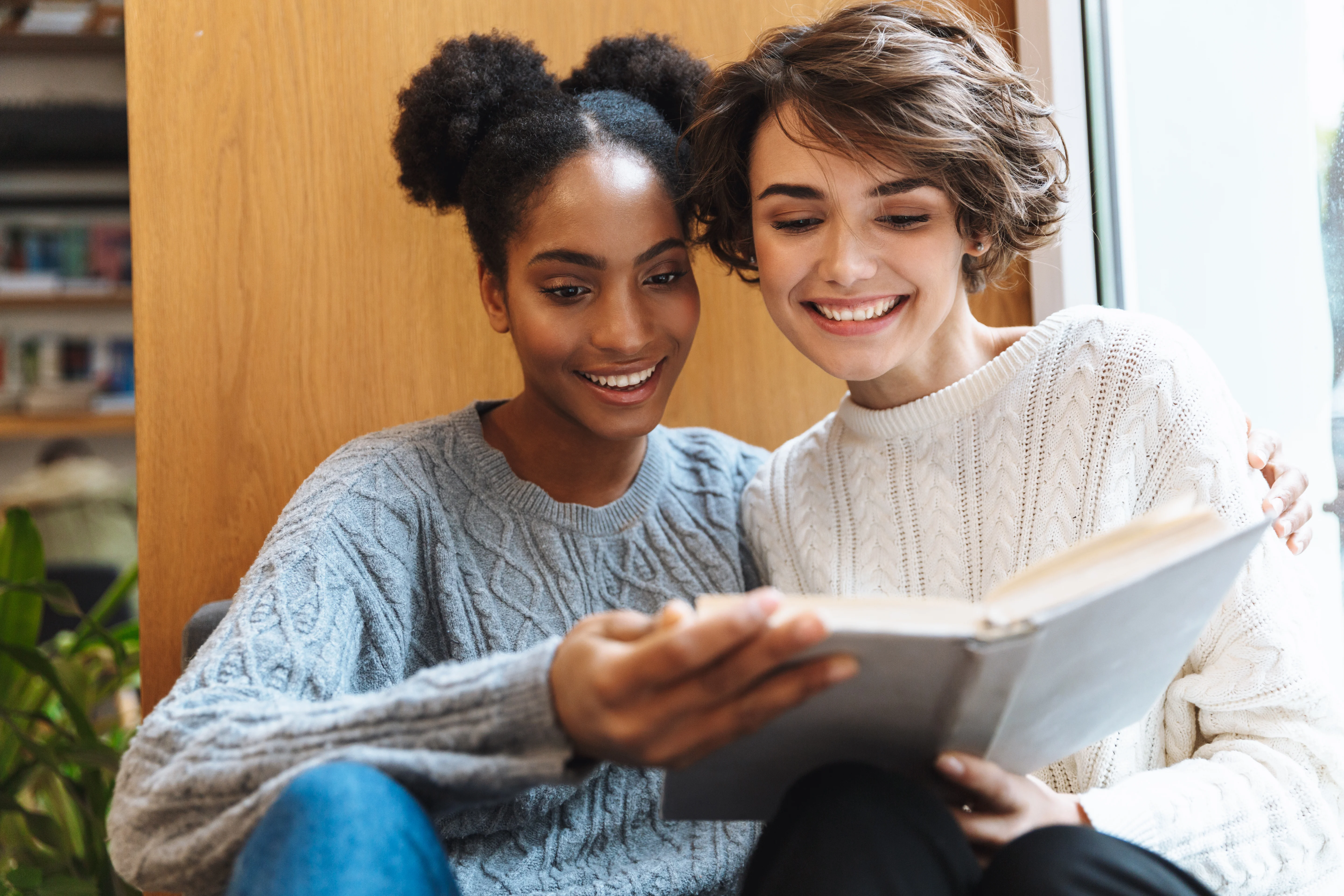 Two girls smiling while reading a book