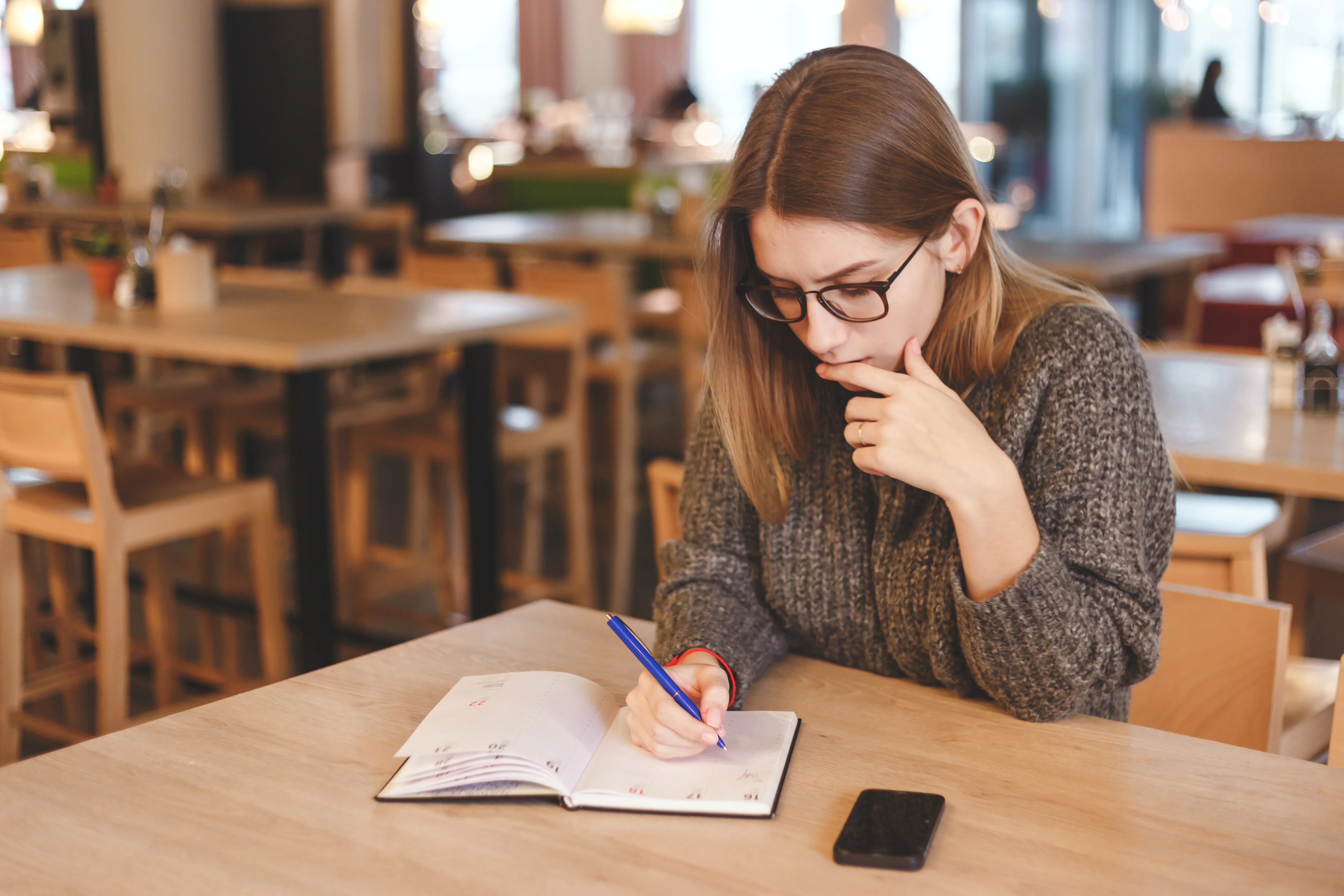 Girl writing in the notebook while sitting at a cafe