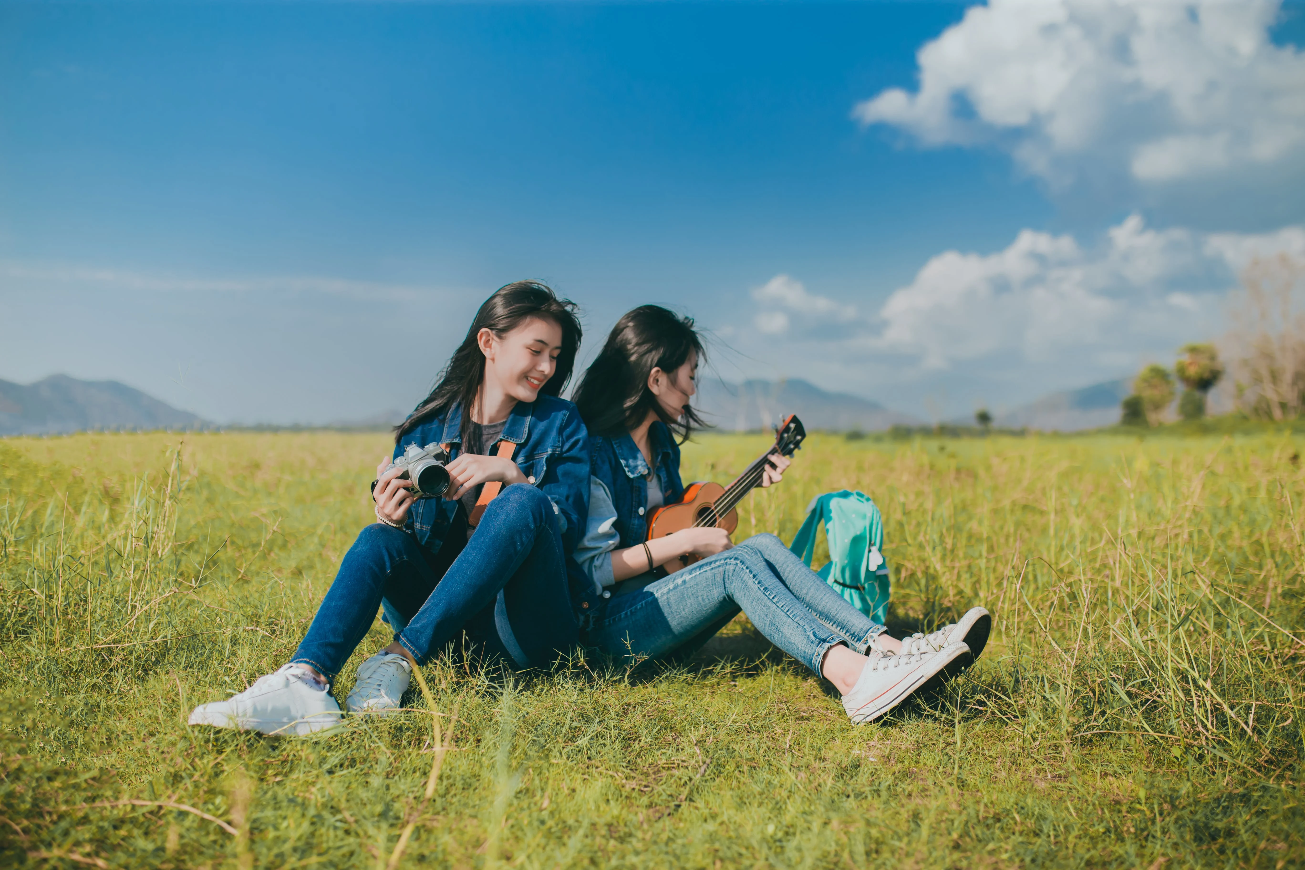 Two girls sitting in a field and playing a guitar