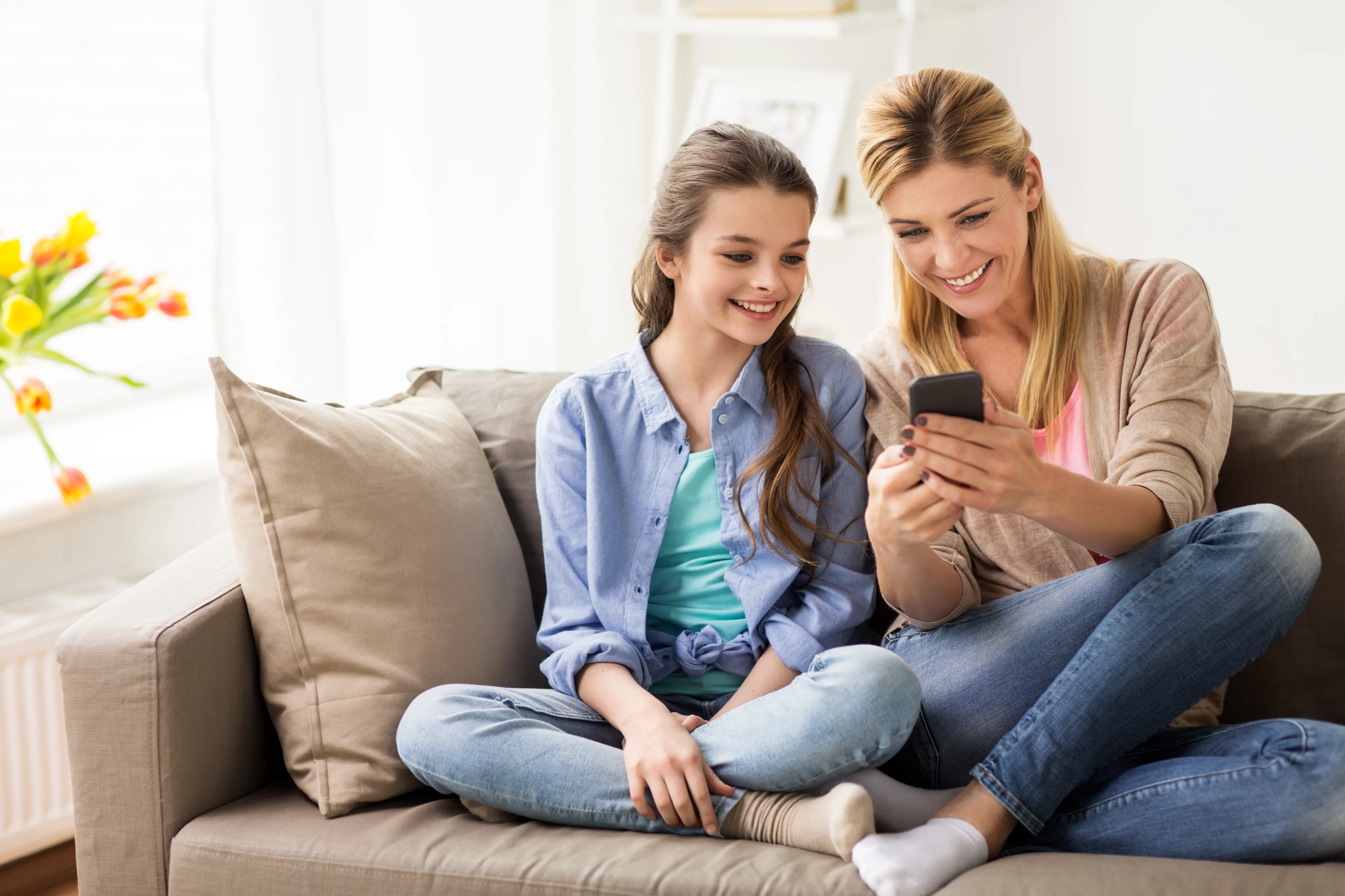 Daughter and mother sitting on a couch while looking at a phone