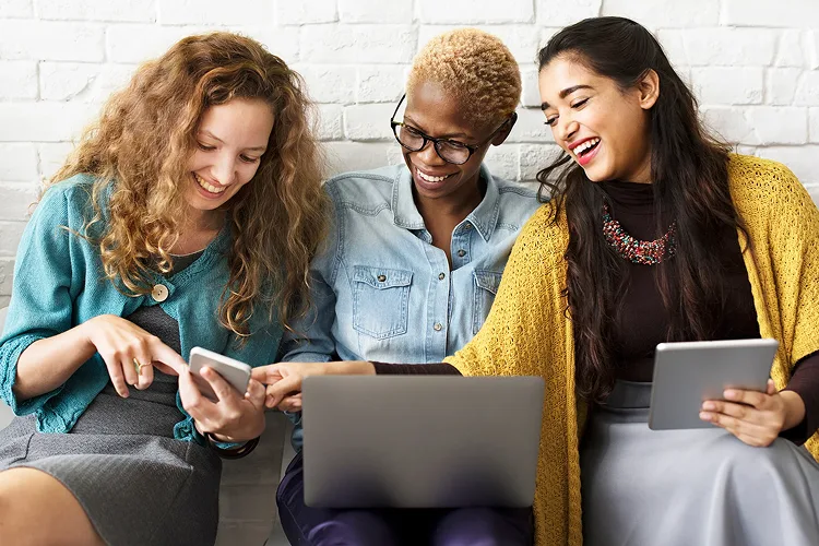 Three women hanging out and watching something on a mobile.