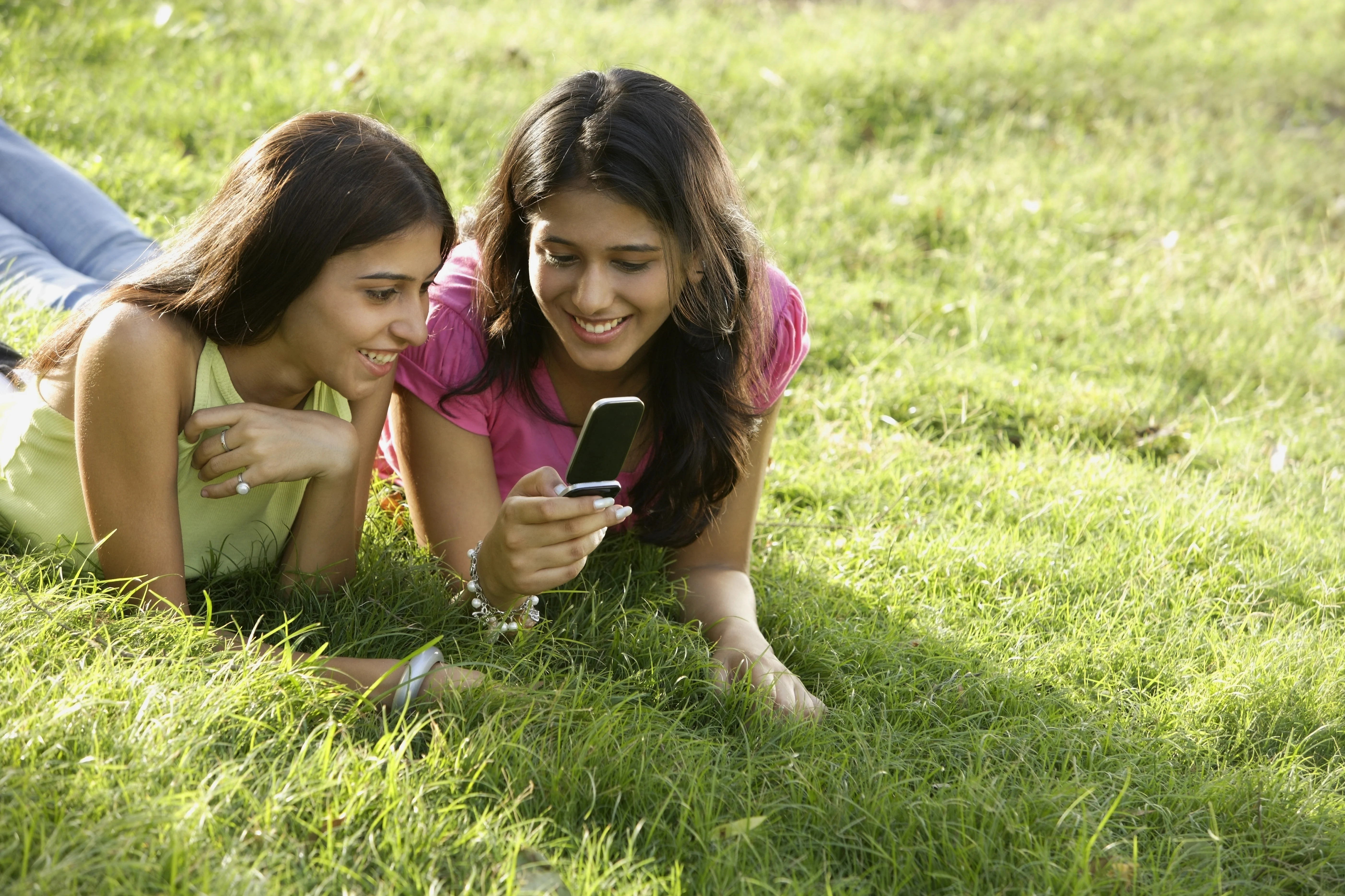 Two girls lying on grass and looking at a phone