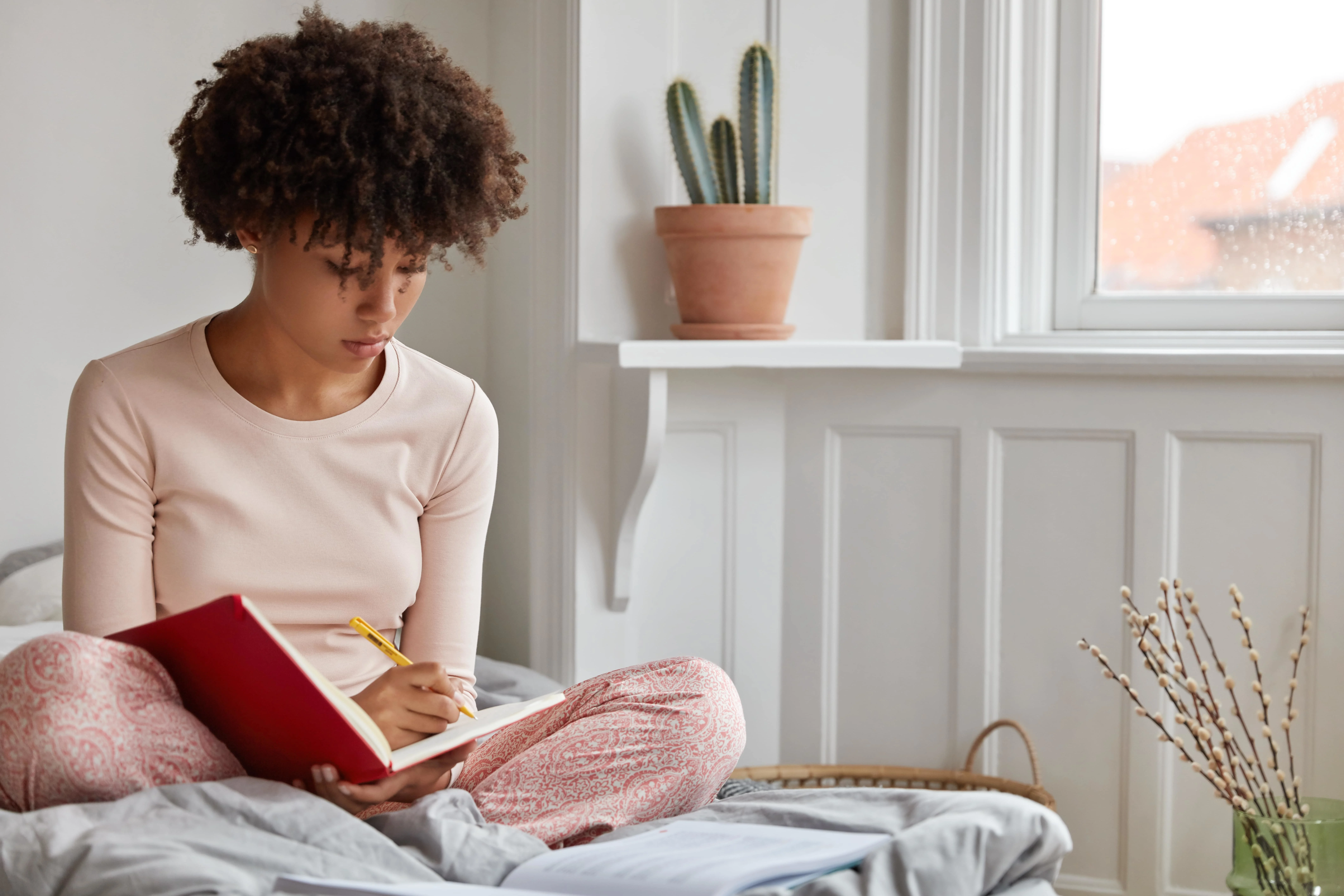 Girl writing in her notebook while sitting on a bed