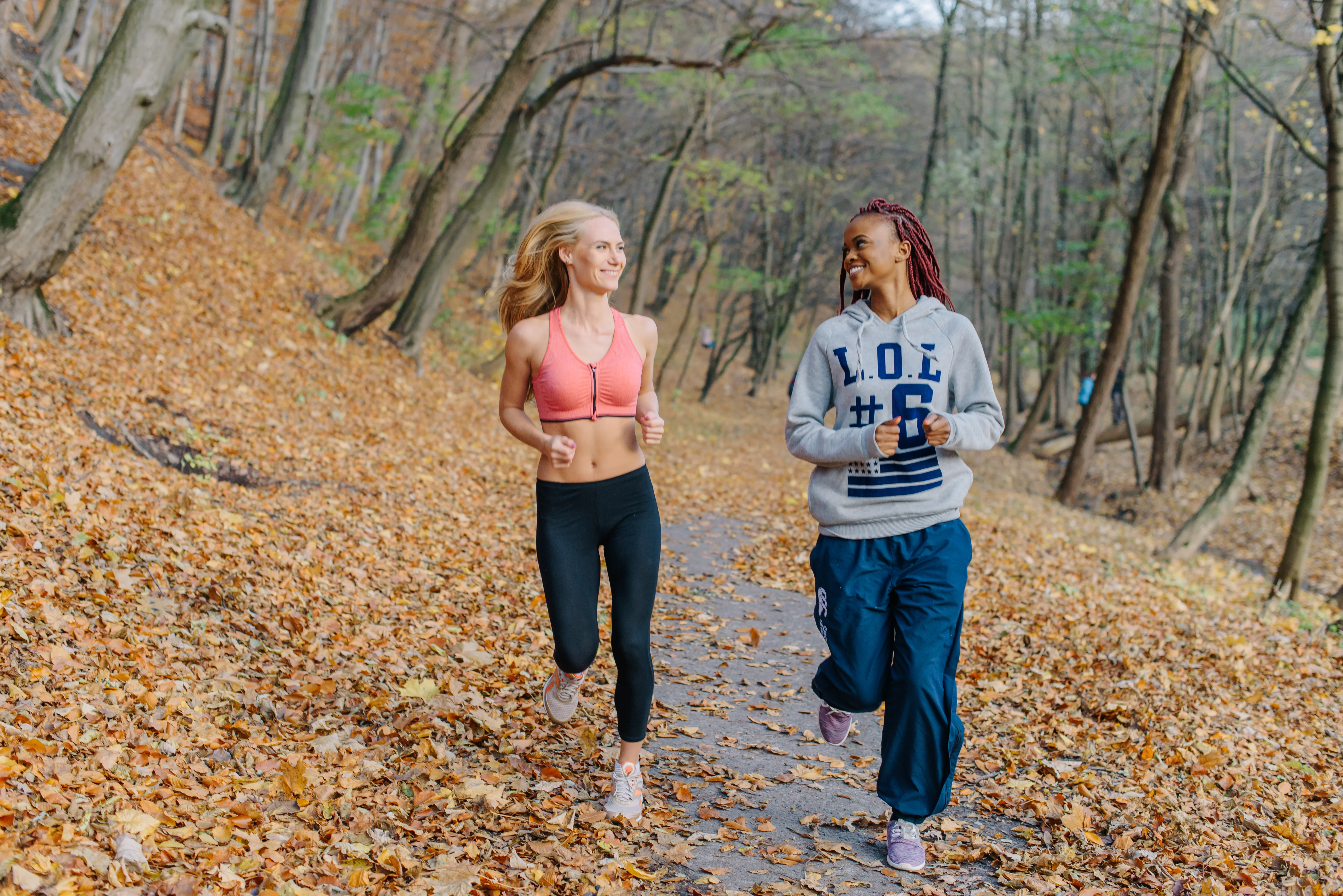 Two women running in the forest and smiling at each other