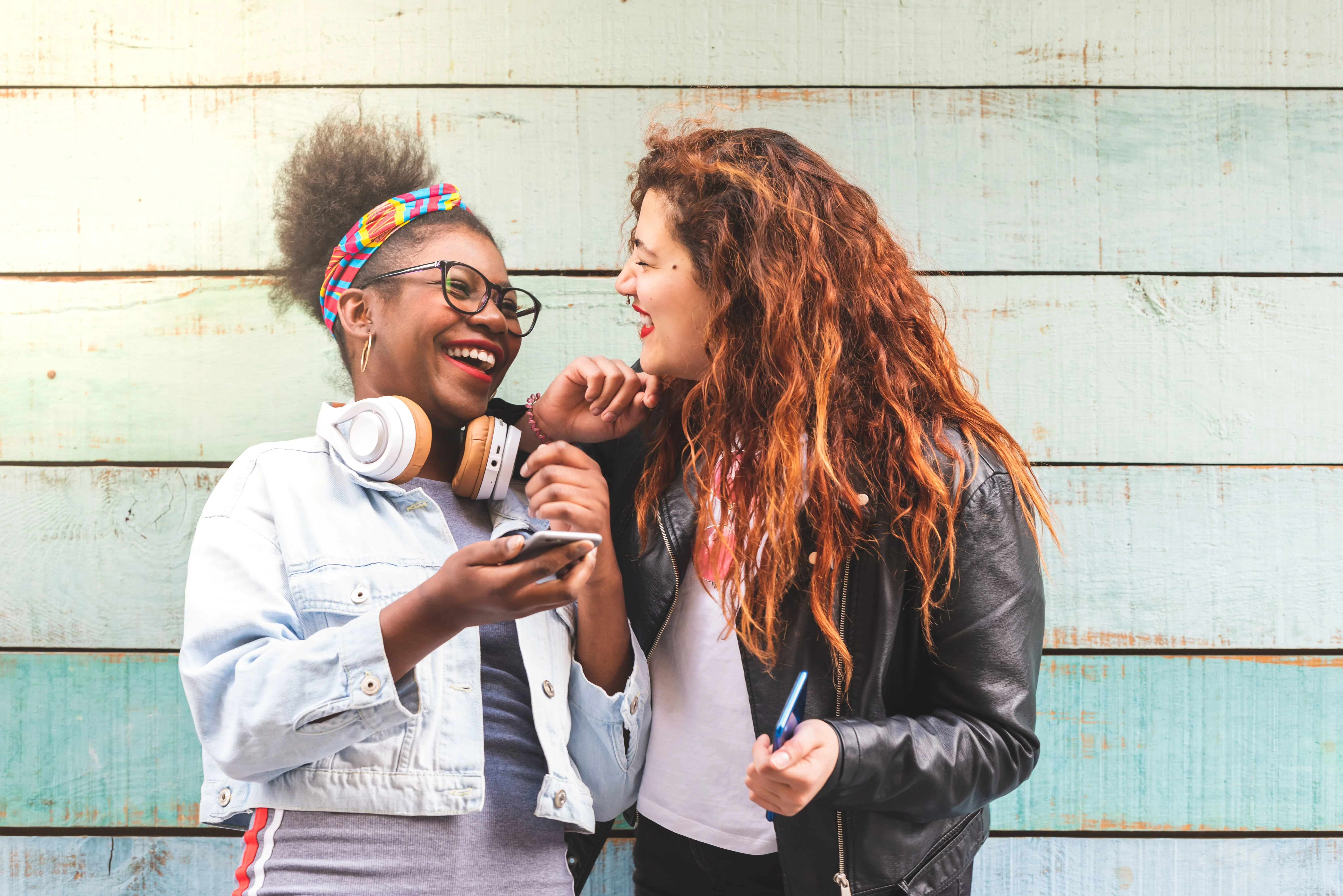 Two girls smiling and looking at each other in front of a wall