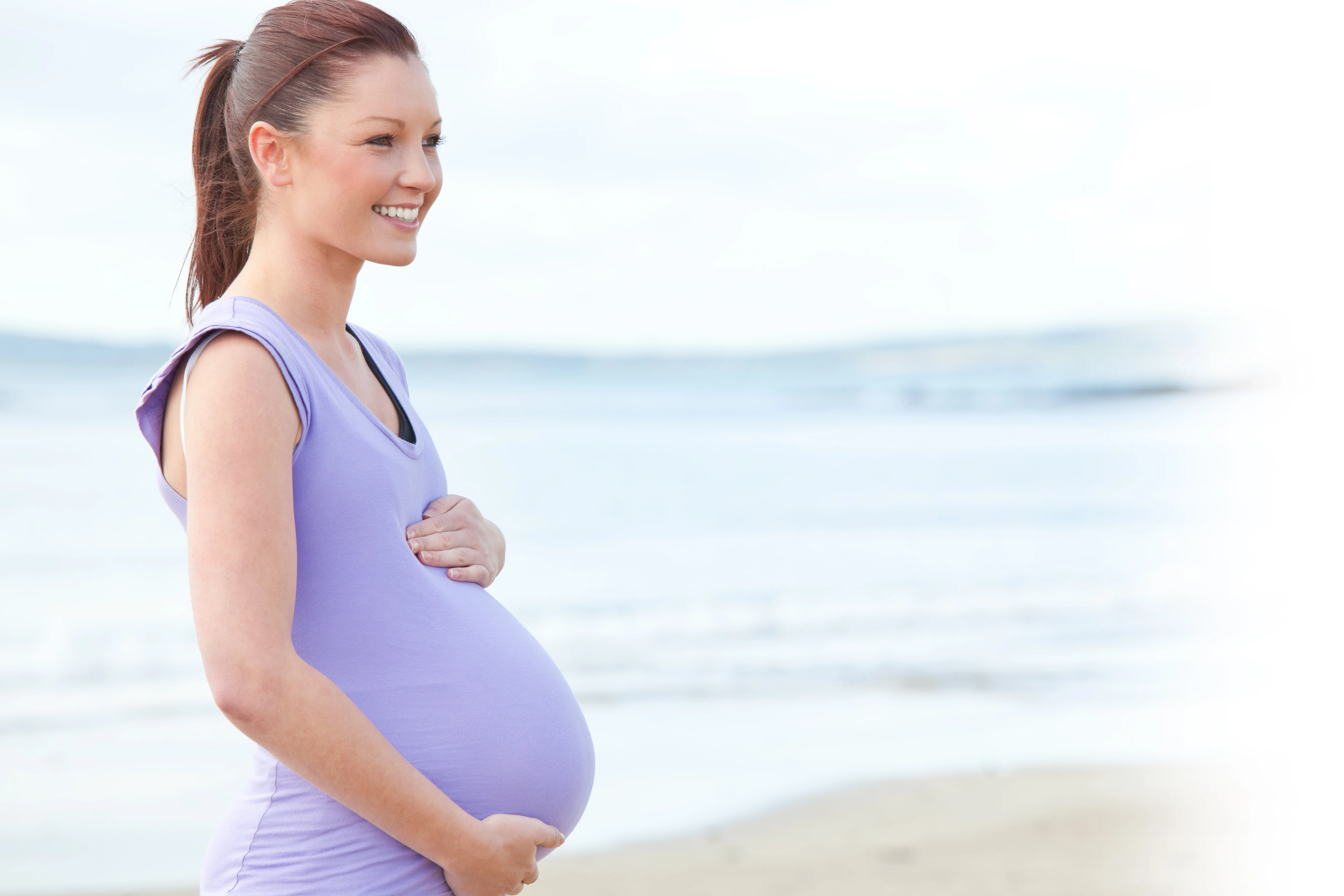 Pregnant woman holding her belly on the beach