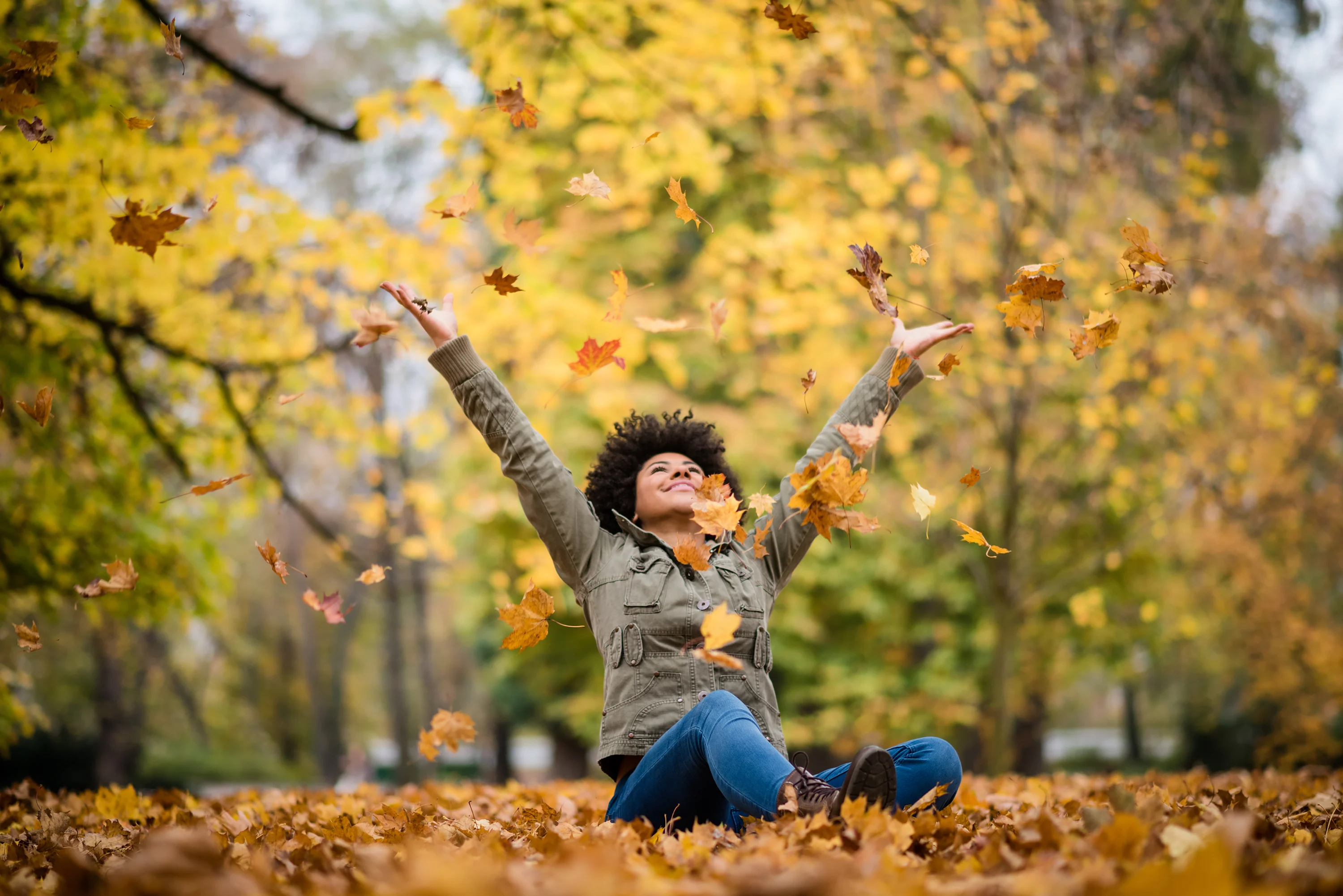 Woman sitting on the ground and throwing autumn leaves into the air