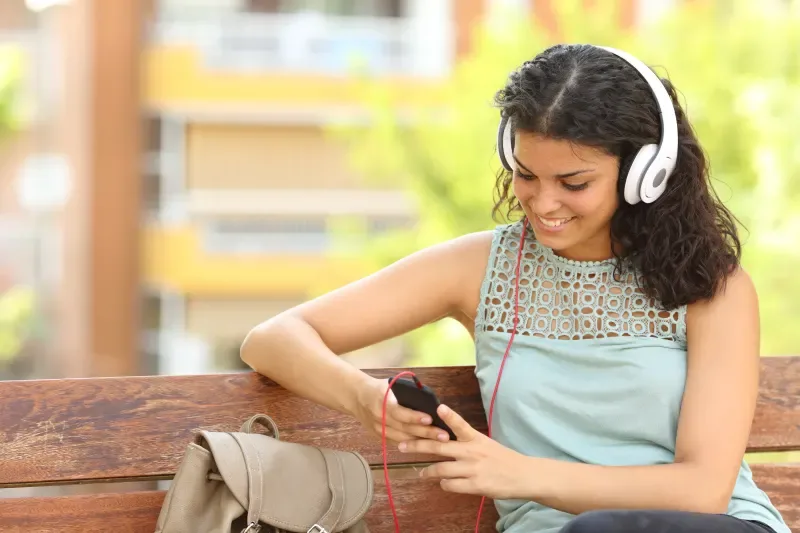 Girl sitting on a bench and listening to music on her phone