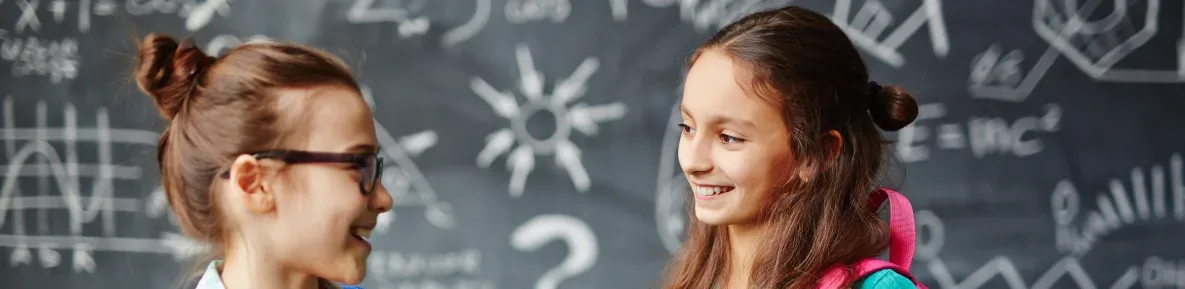 Two girls smiling at each other in front of a black board