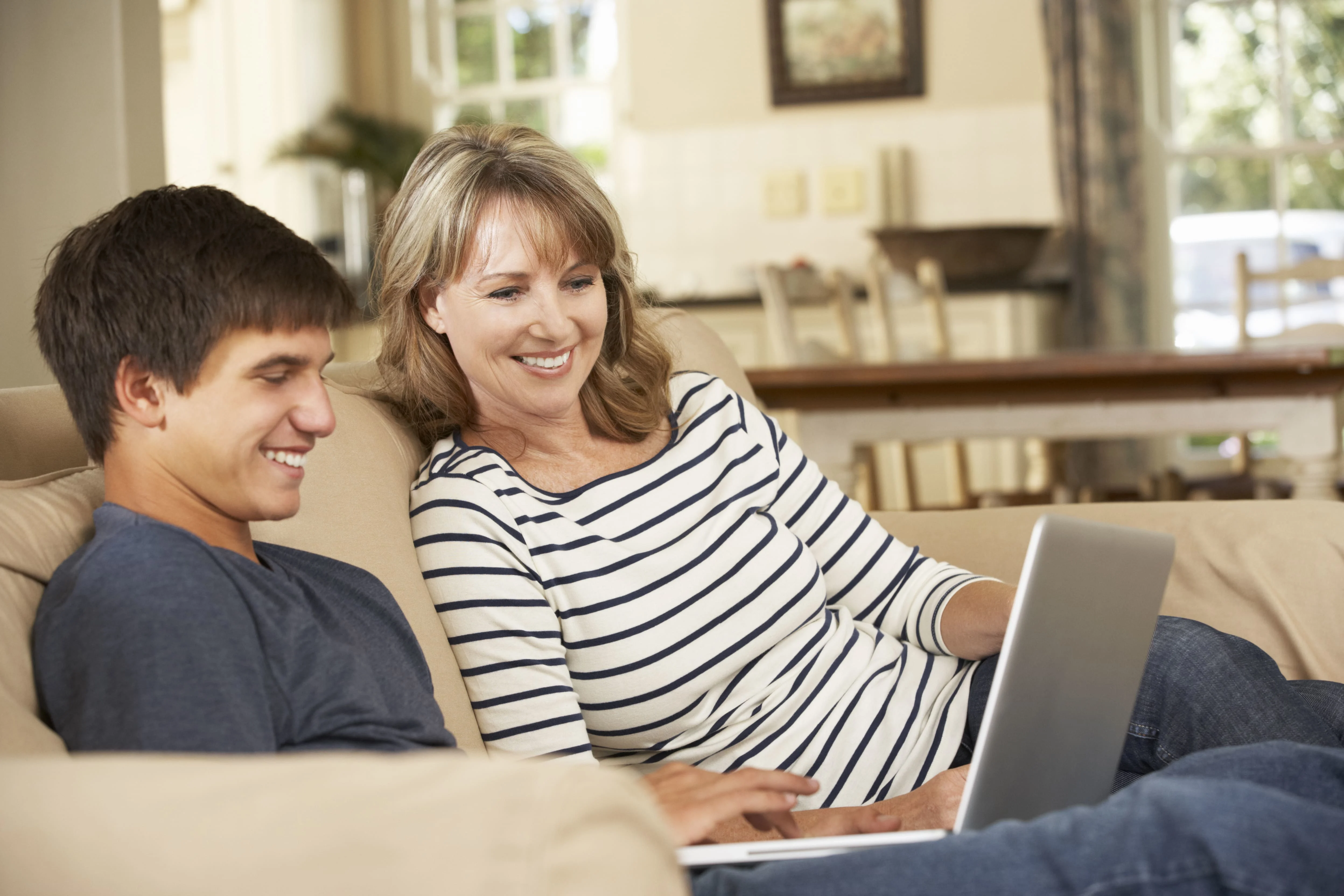 Son and a mother sitting at a couch and looking at a laptop screen