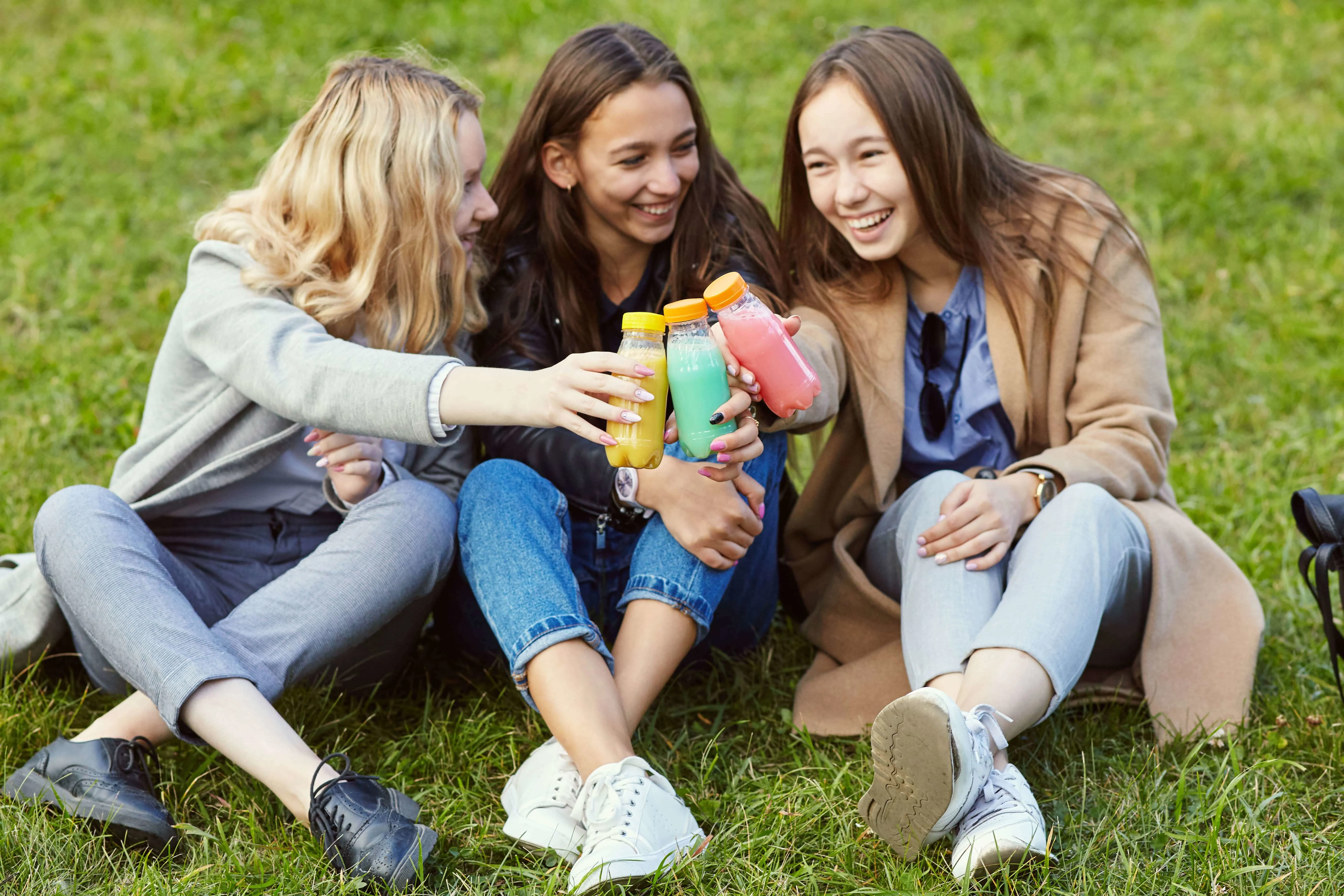Three girls sitting on a grass cheering with the juices