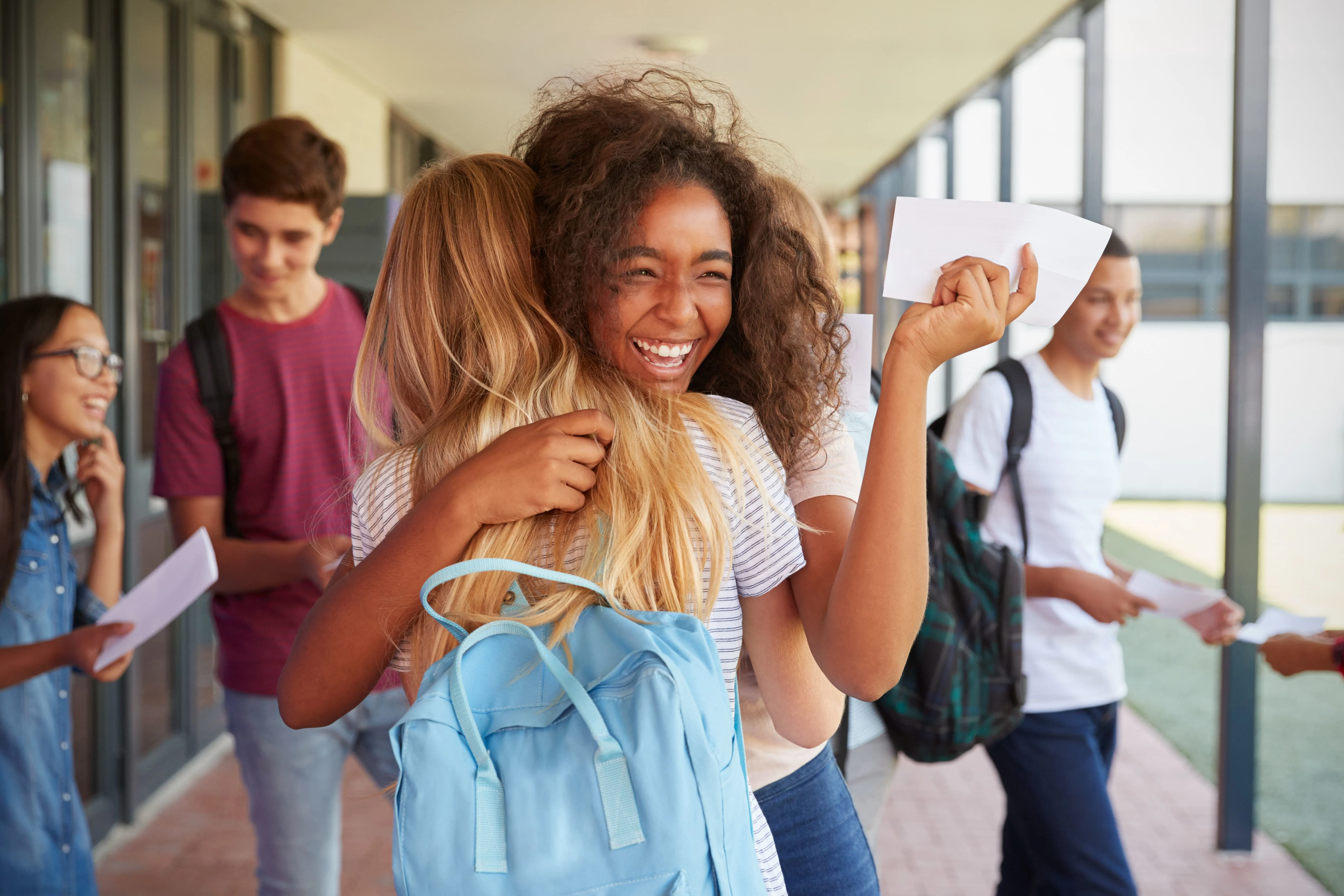 Two girl friends in hallway at school hugging