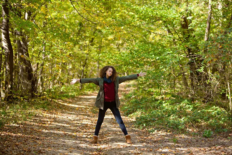 Woman standing in a autumn forest pathway with her arms wide open