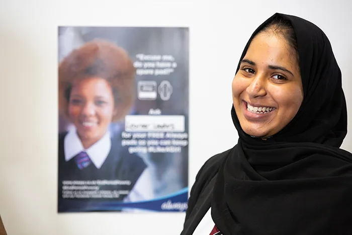 Portrait of a girl smiling standing in front of a End Period Poverty poster