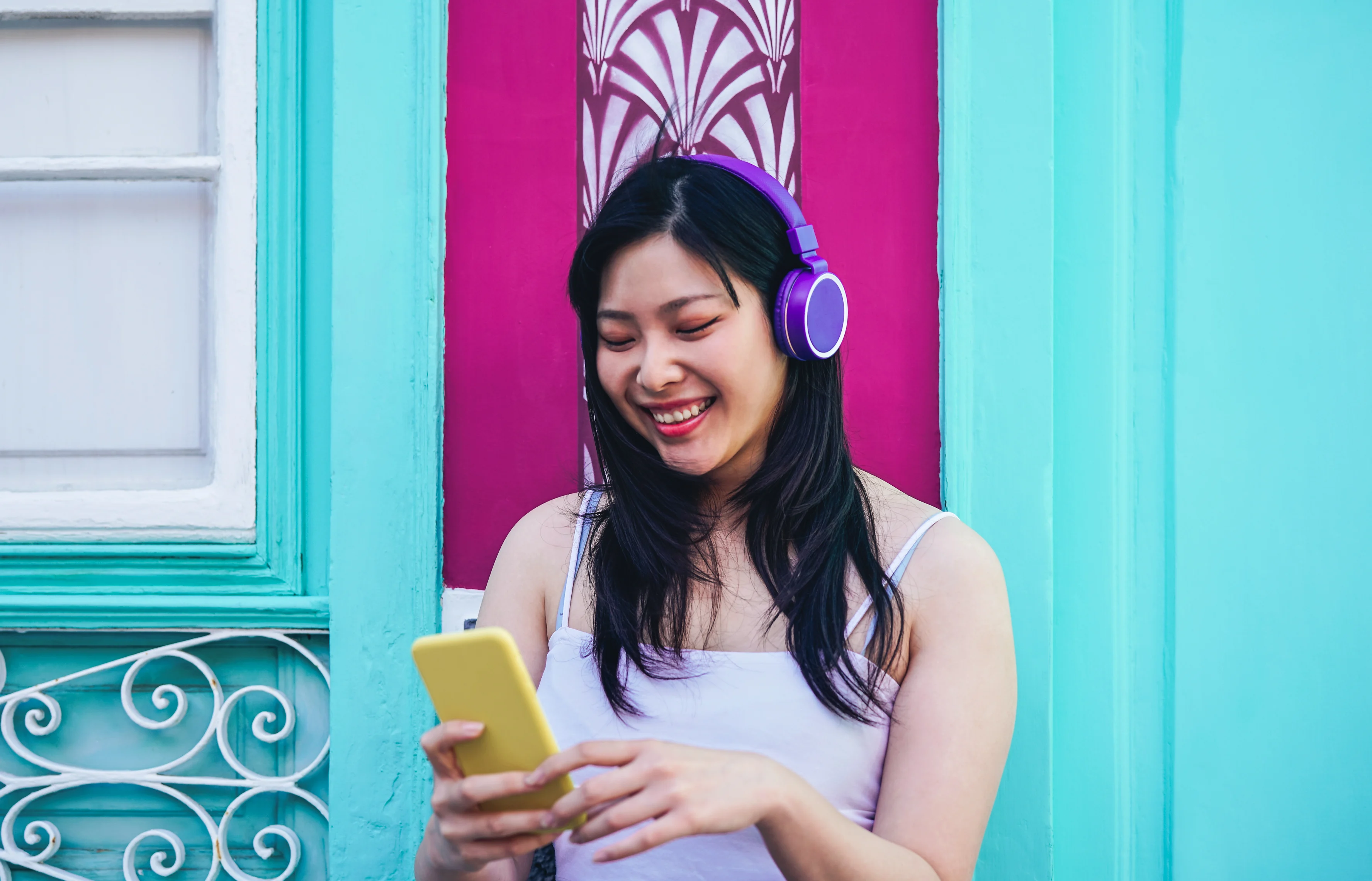 Girl with headphones looking at her phone in front of a turquoise and purple wall