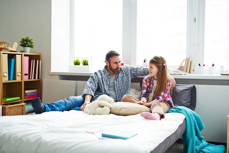 Father and daughter talking while sitting on a bed