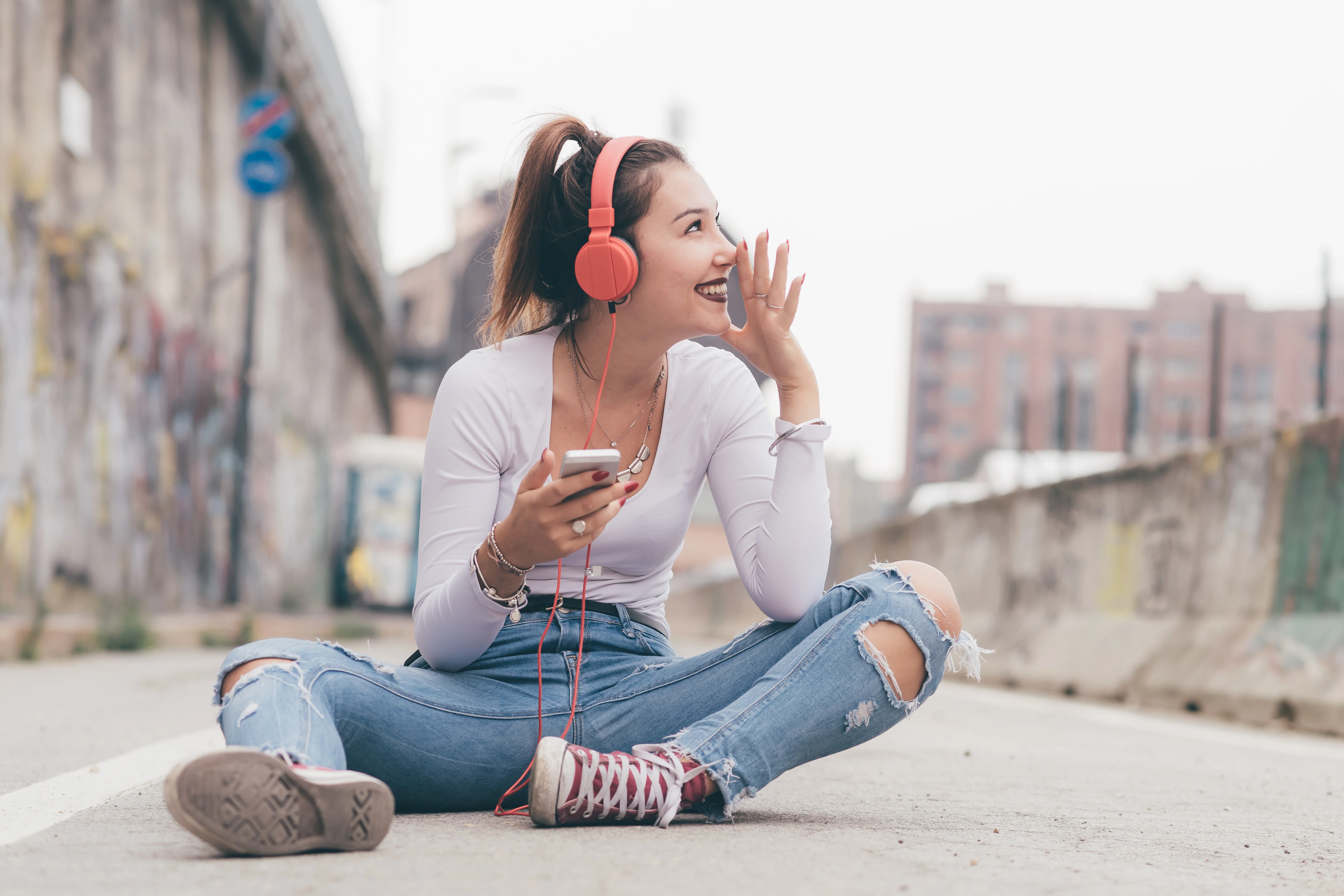 Girl sitting on the ground outside smiling and listening to music