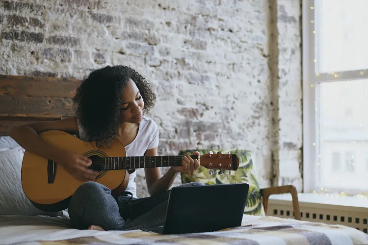 Girl playing a guitar while sitting on a bed