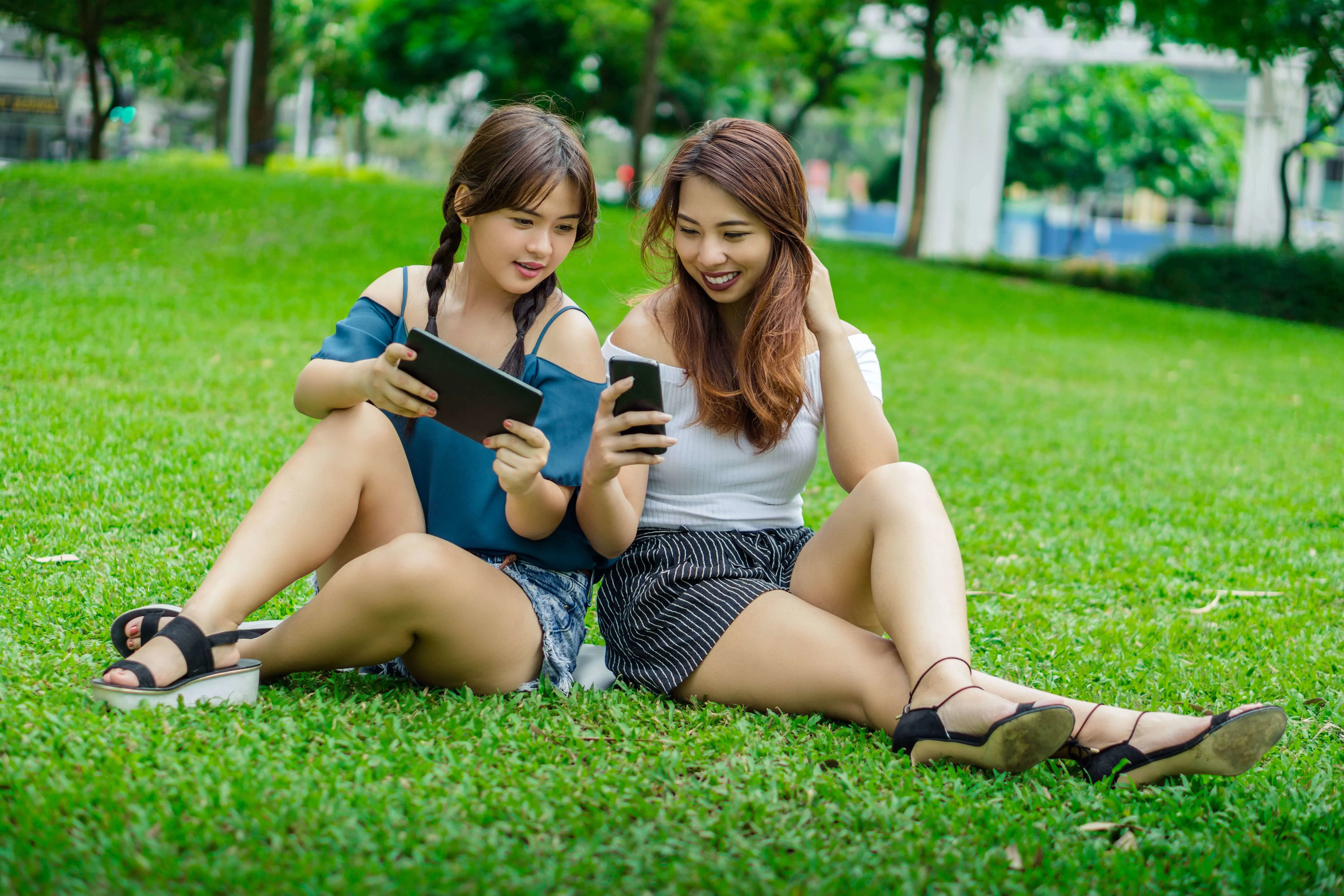 Two girls sitting on grass and looking at their phones