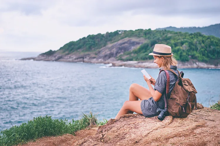 Woman sitting on a rock on the beach and reading a book