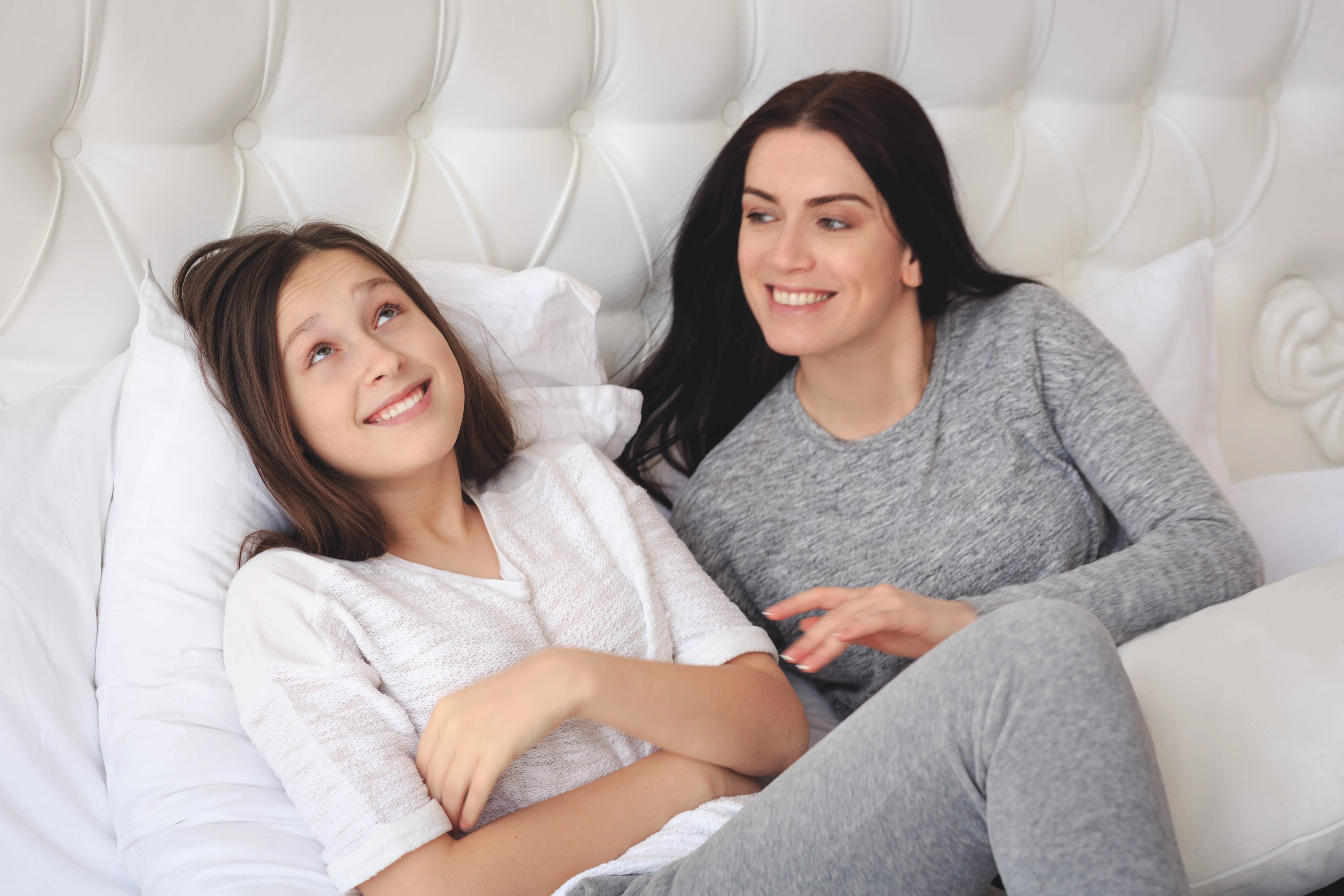 Mother and daughter smiling while lying on the bed