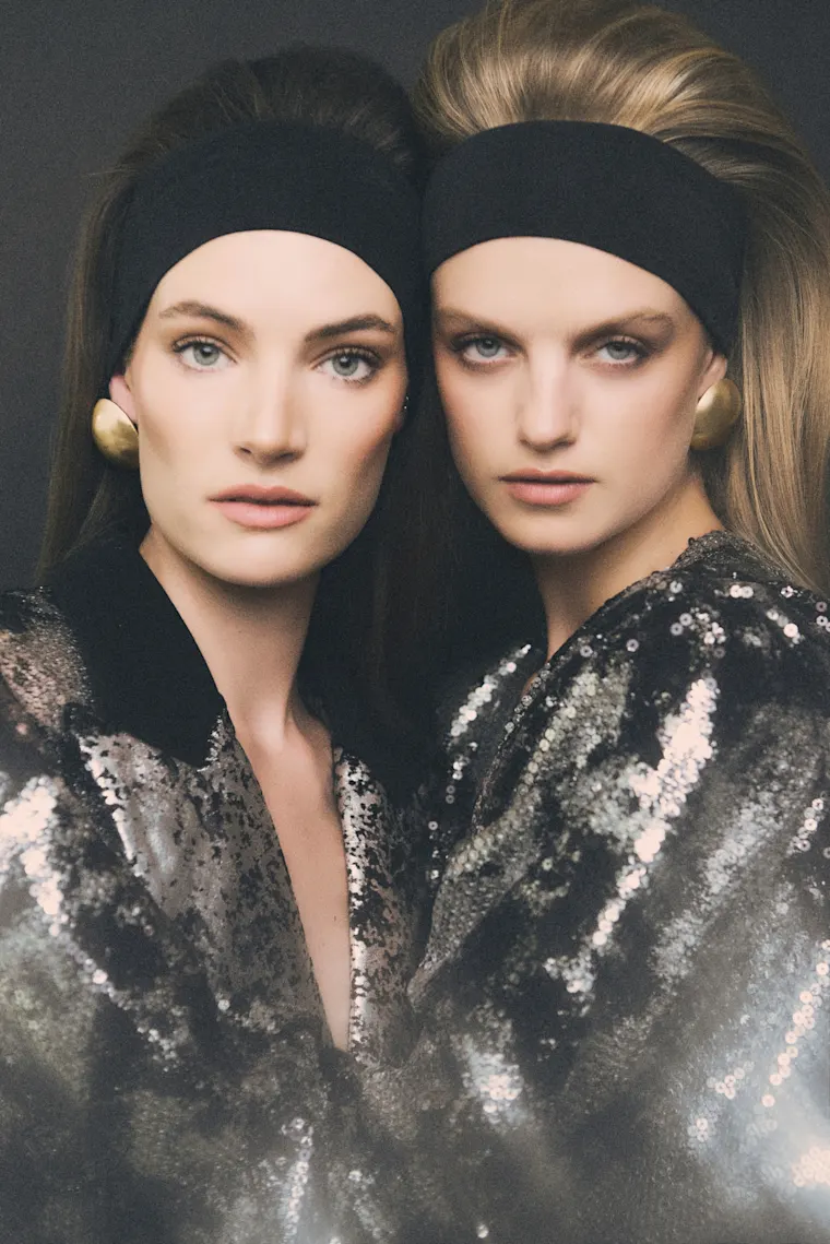 Dos modelas con diademas negras y sacos de lentejuelas sobre fondo oscuro