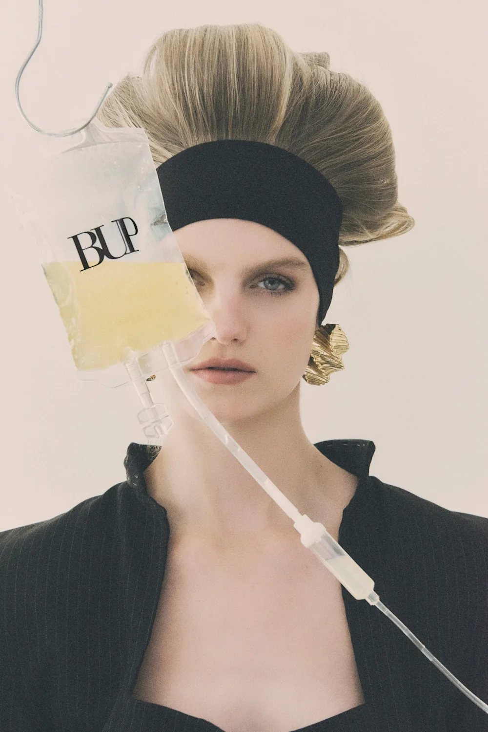 Modelo con diadema negra y saco de sastre junto a una bolsa de suero rotulada BUP, imagen conceptual de la campaña