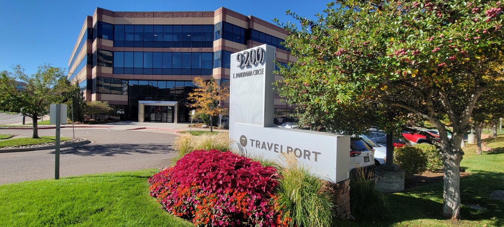 Travelport's Denver office. The office building next to a Travelport sign surrounded by flowers, green grass, and budding trees.