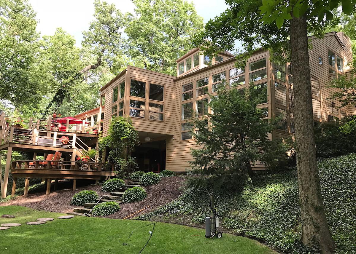 A tan home with many windows from below with trees all around
