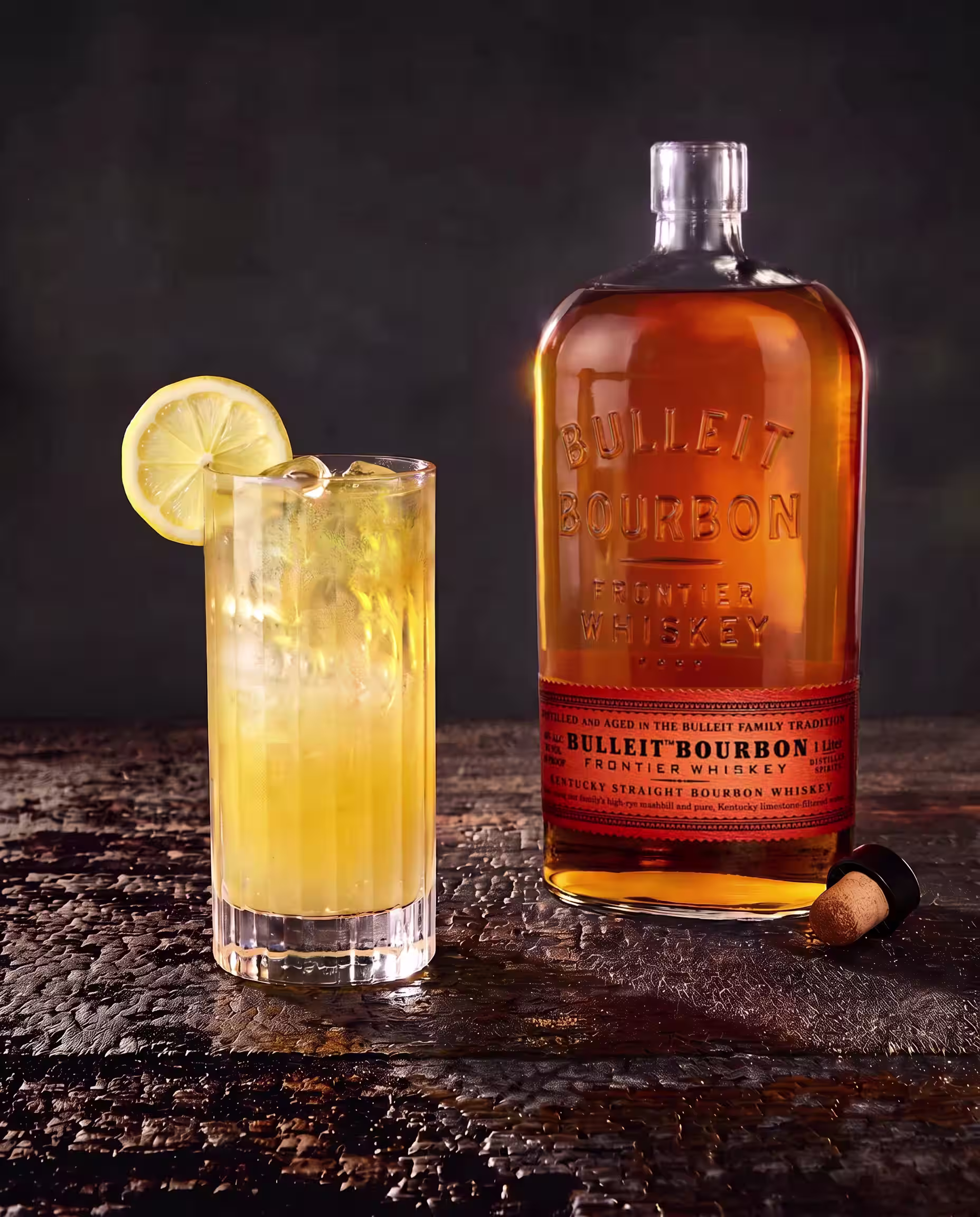 Bulleit Bourbon bottle beside a whiskey cocktail with ice and lemon garnish