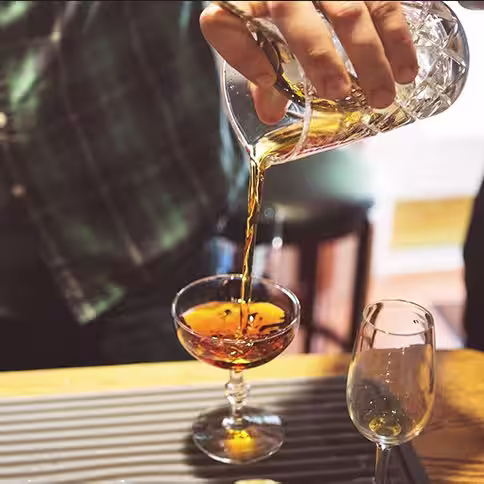 A bartender pours cocktail into small round glass