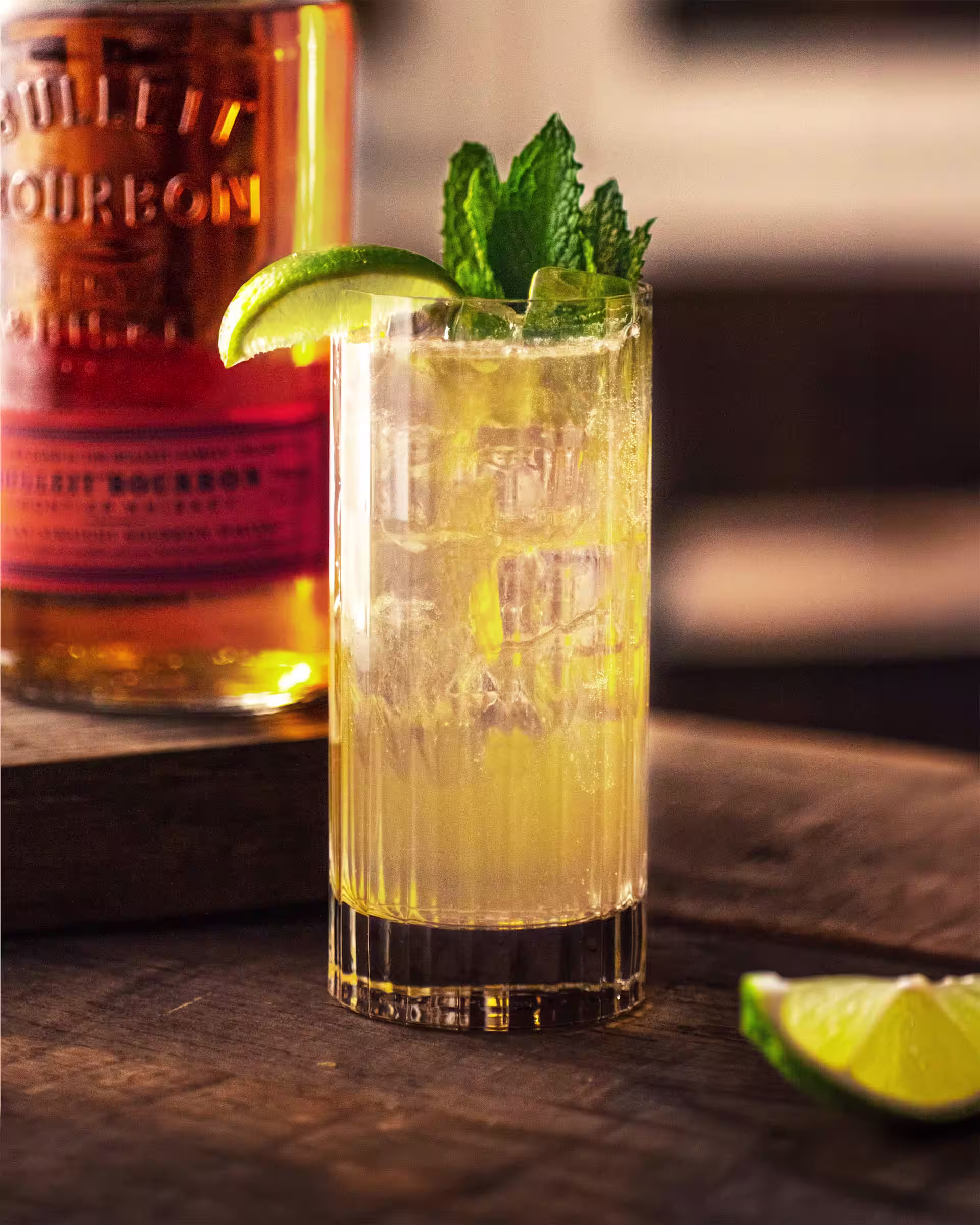 Kentucky Mule cocktail with ice, lime and fresh mint beside a Bulleit Bourbon bottle