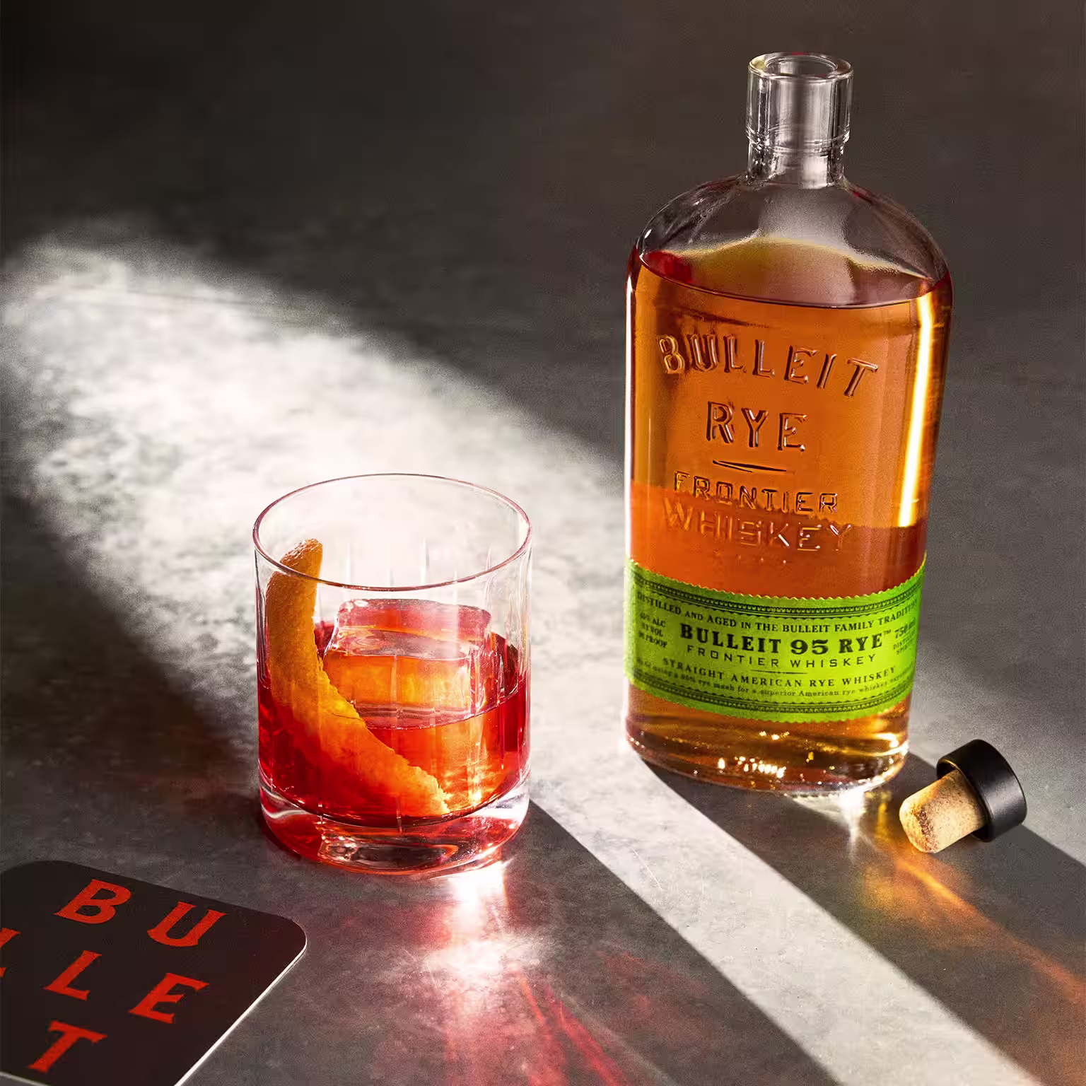 Two Bulleit cocktails with orange peel and cherry against a red background