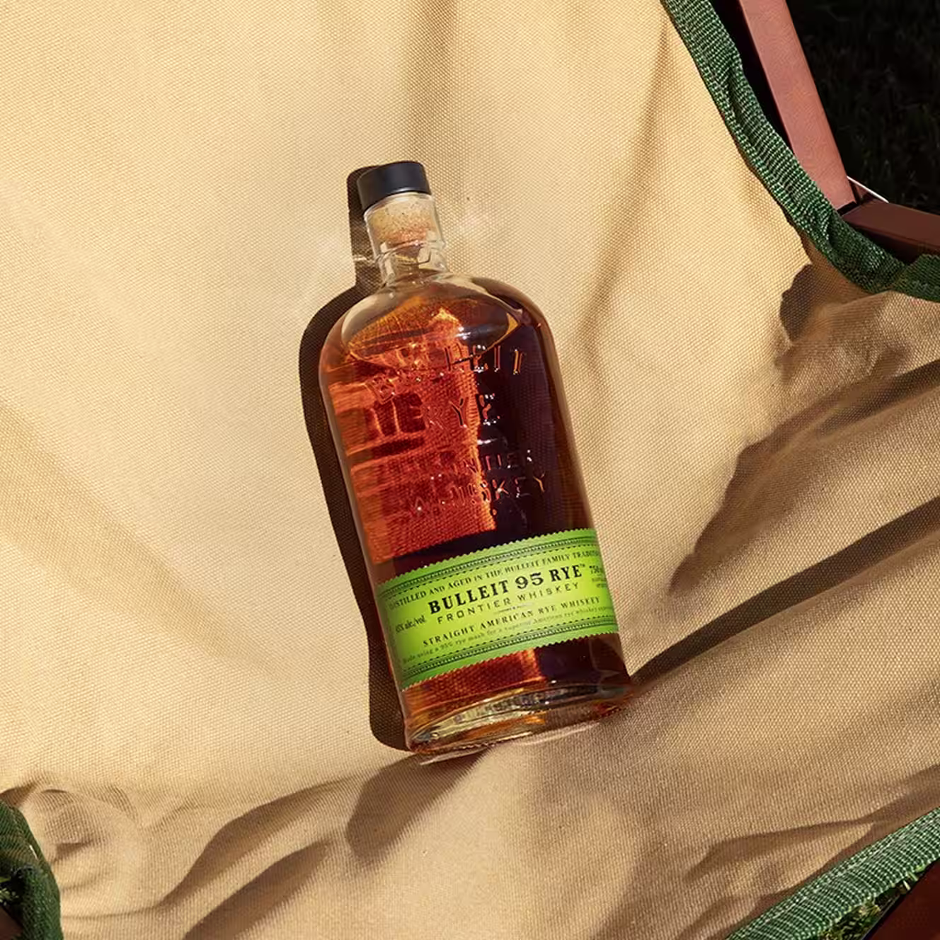 Bulleit 95 Rye whiskey bottle resting on a canvas chair in sunlight