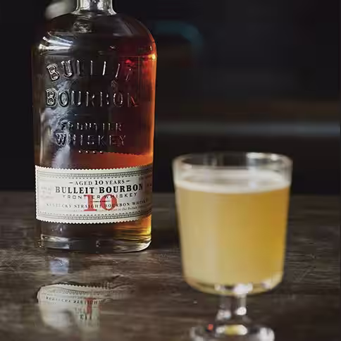 A bottle of Bulleit 10 Year behind a small cocktail glass