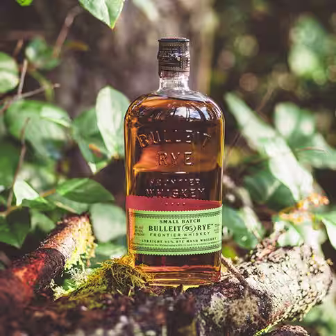 A bartender pouring Bulleit Bourbon into a cocktail shaker