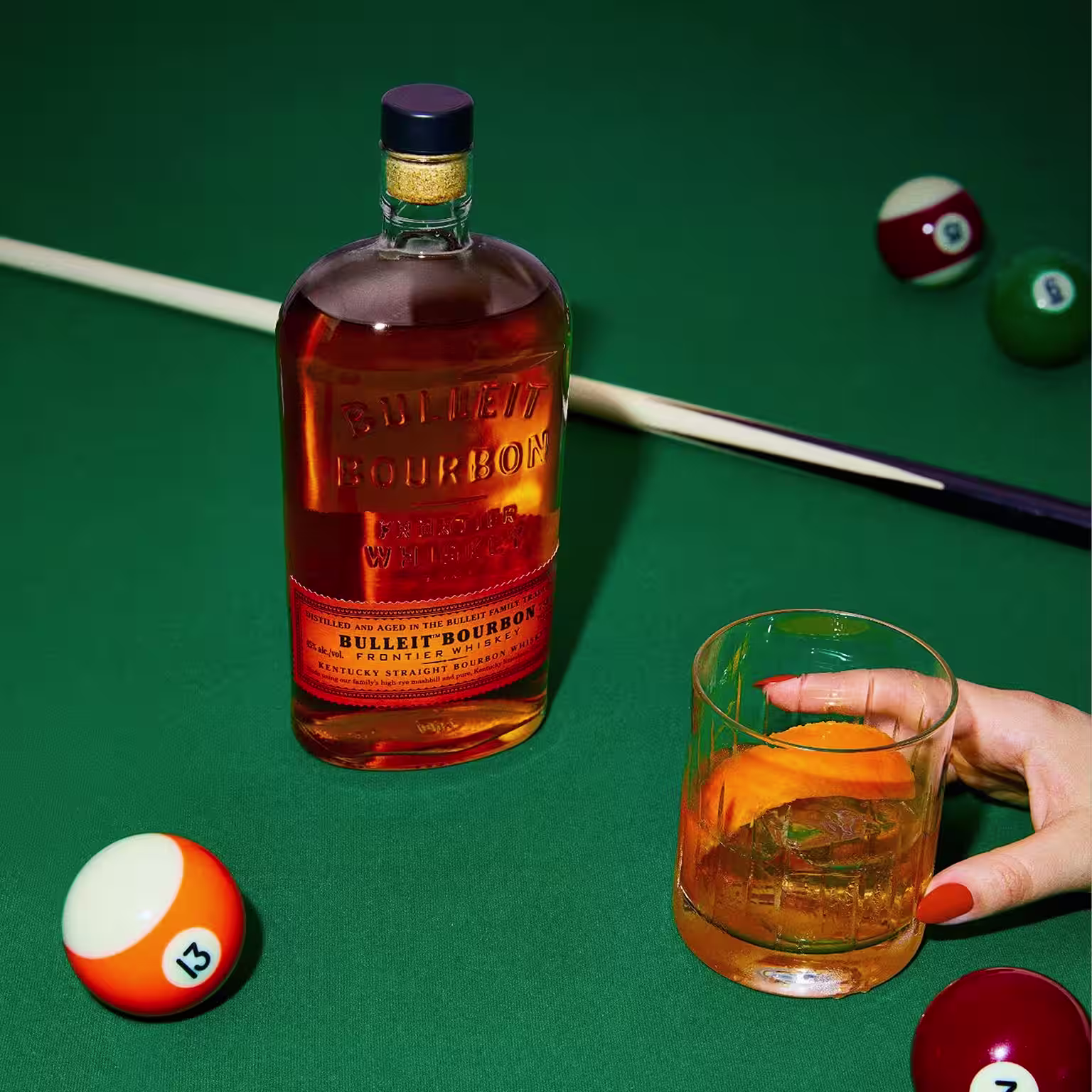 Bulleit Bourbon bottle and whiskey cocktail on a green pool table with billiard balls