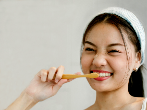 Young adult woman in white headband holding toothbrush to her front teeth