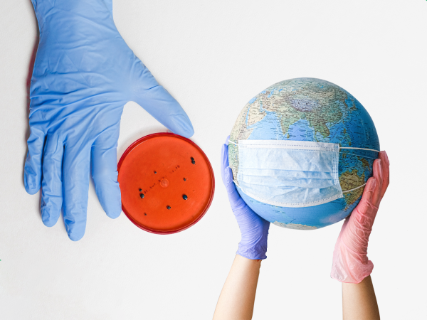 Picture of a gloved hand holding a Petri dish and another set of gloved hands holding a globe with a mask on it