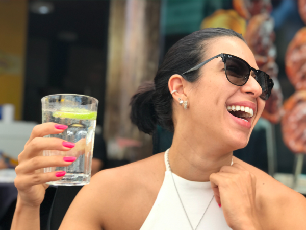 Woman wearing sunglasses and smiling, holding a glass of sparkling water with a lime