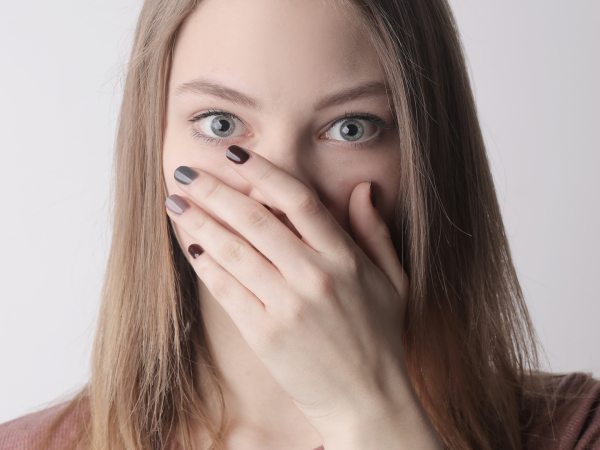 Young woman with painted fingernails covering her mouth with her hand.