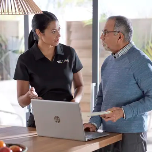 News - Geek Squad agent speaking with a man in his home while they are both standing in front of his laptop