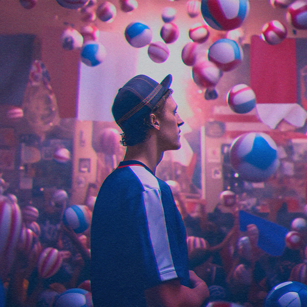 Image of a young man in blue t-shirt and blue cap against pink background in which balls are flying around.