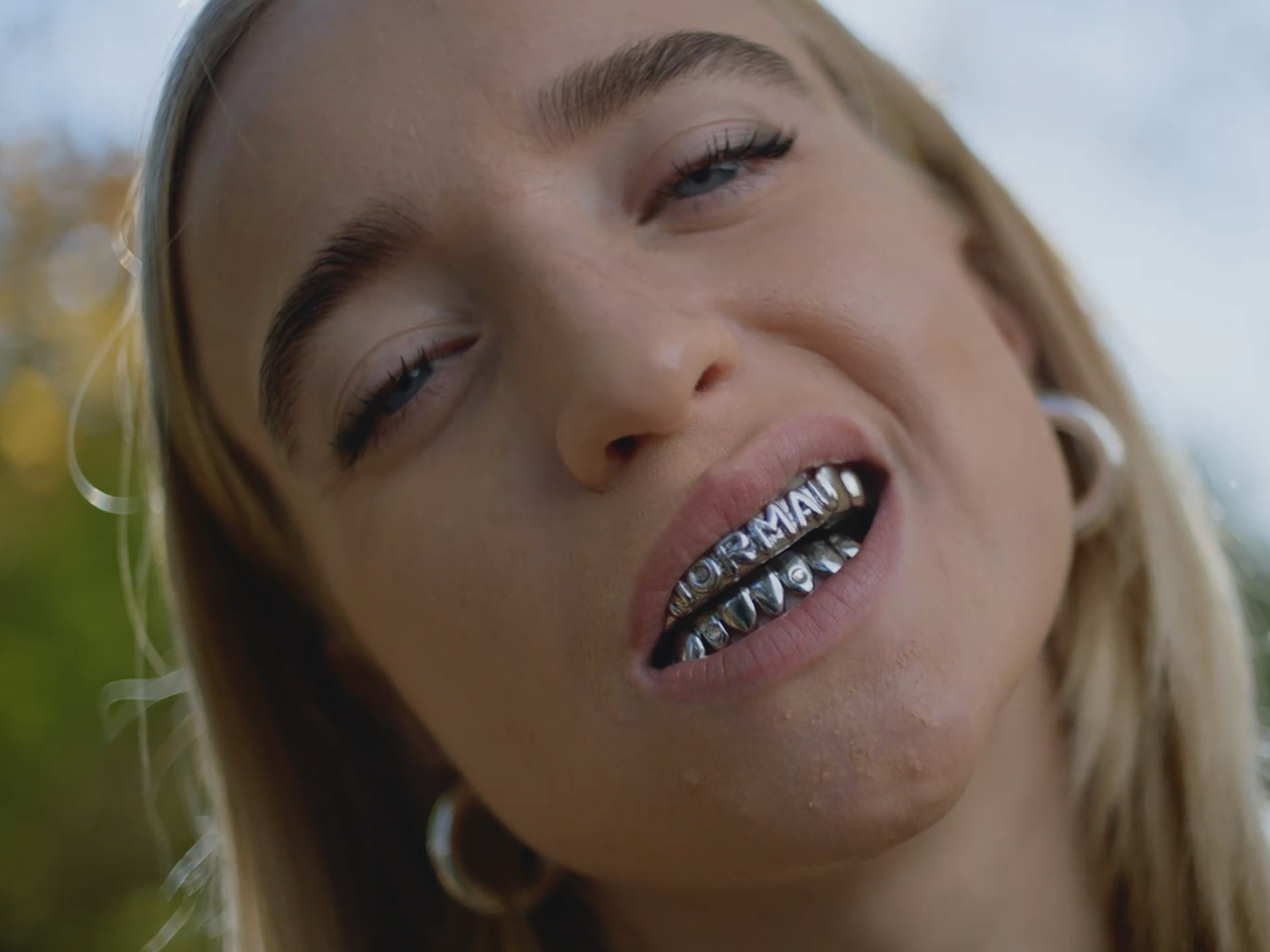 Image of the face of a blonde woman with grillz. The image is part of the image campaign "ist doch ganz normal" by Jung von Matt LIMMAT for PostFinance.