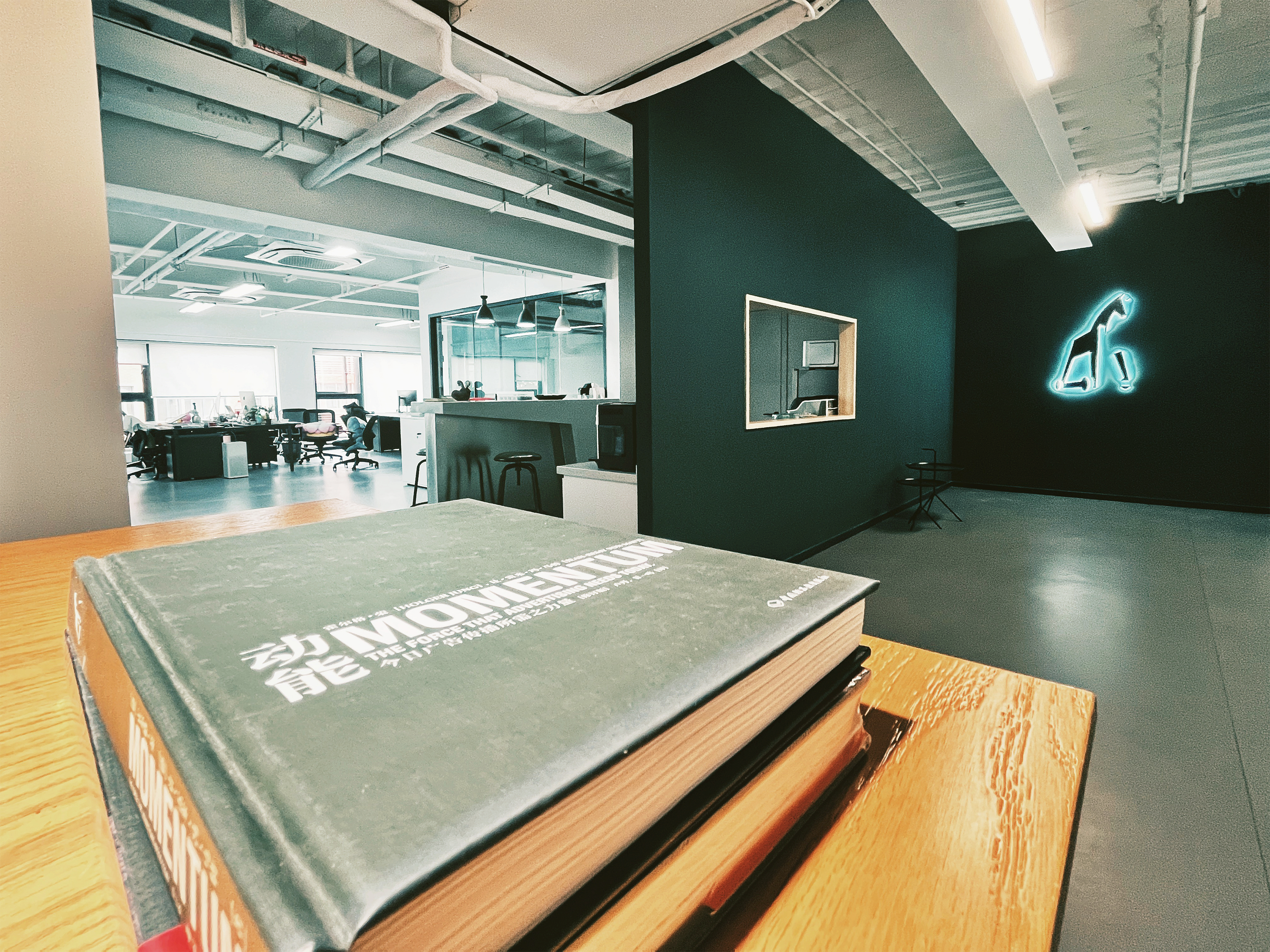 Image from inside the modern office of Jung von Matt Shanghai. In the foreground a book with "Momentum" written on it. In the background desks and computers.