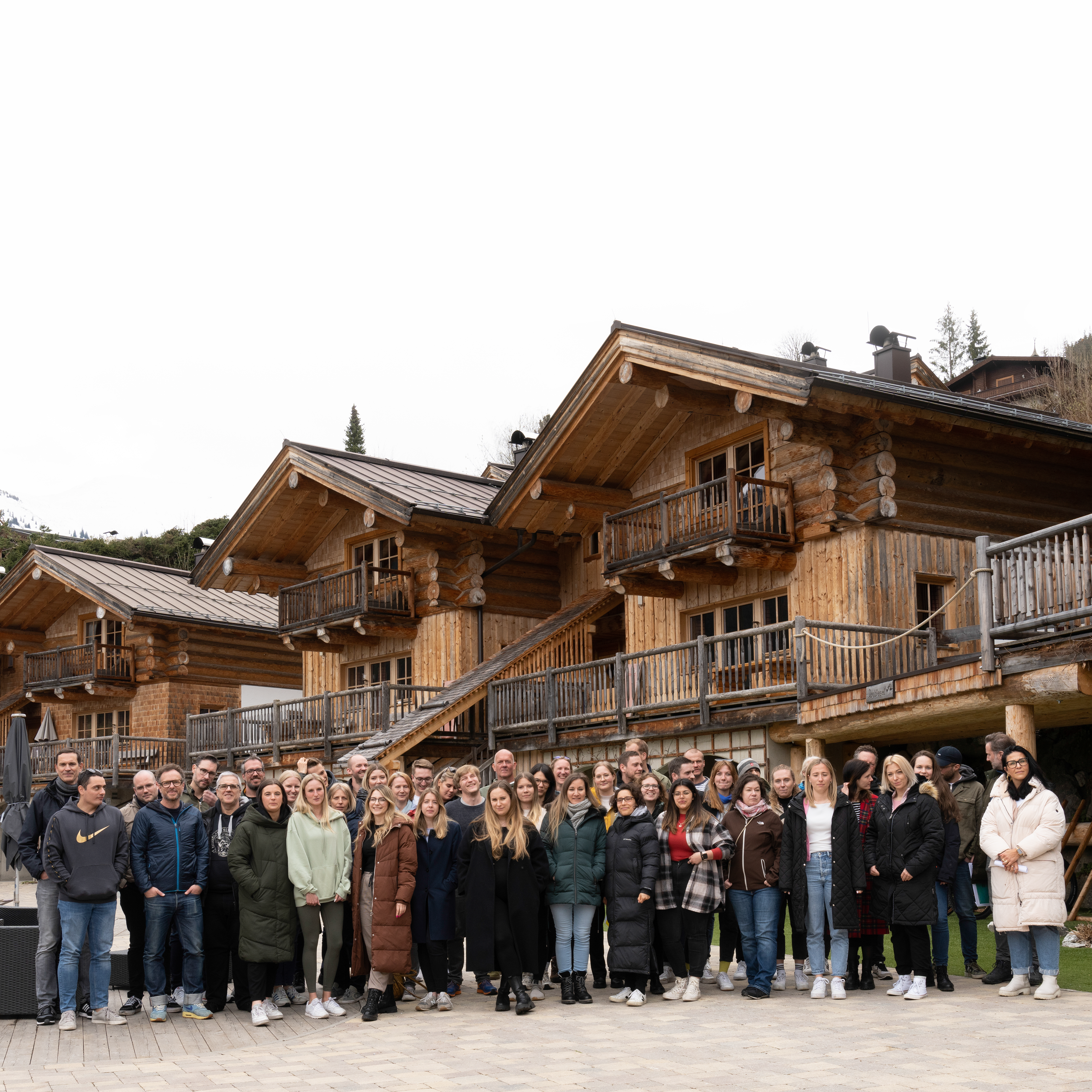 Picture of many employees of the Jung von Matt Netzeffekt office. In the background bavarian, wooden accommodation and a mountain can be seen.