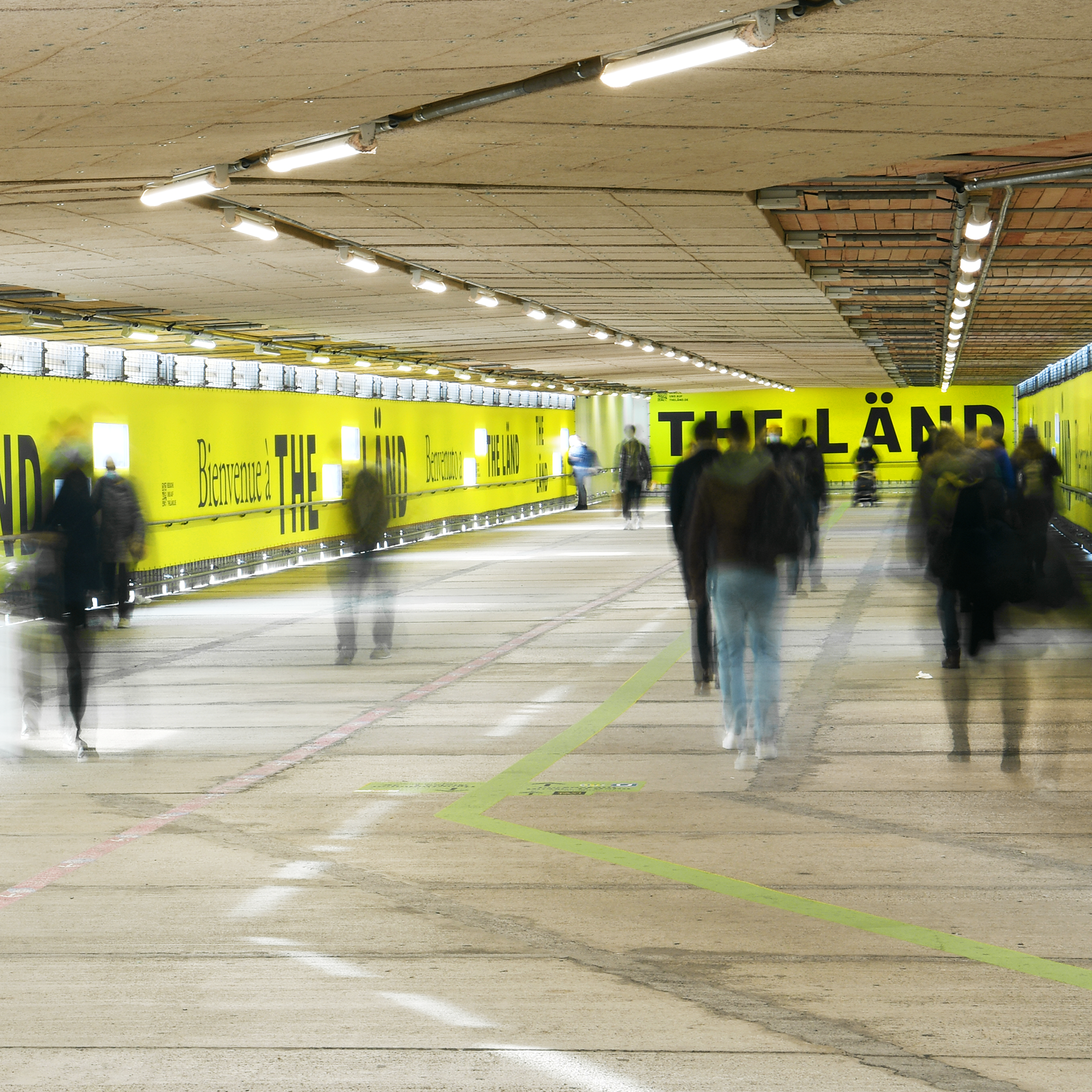about 10-15 people walk through a kind of illuminated tunnel. the walls are placarded with the branding of The Länd.