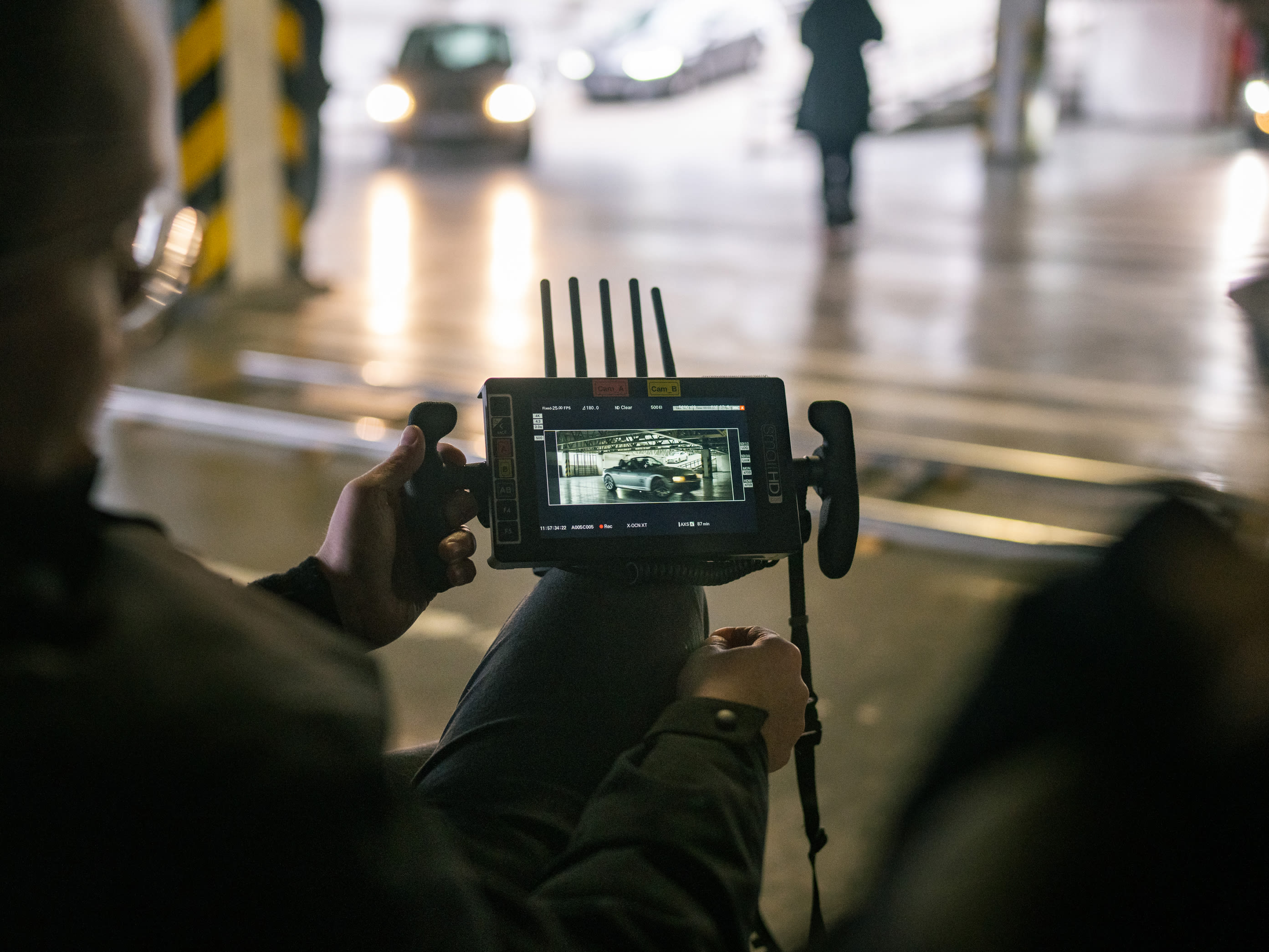 A man stands in front of a car, holding a camera and ready to capture the perfect shot. 