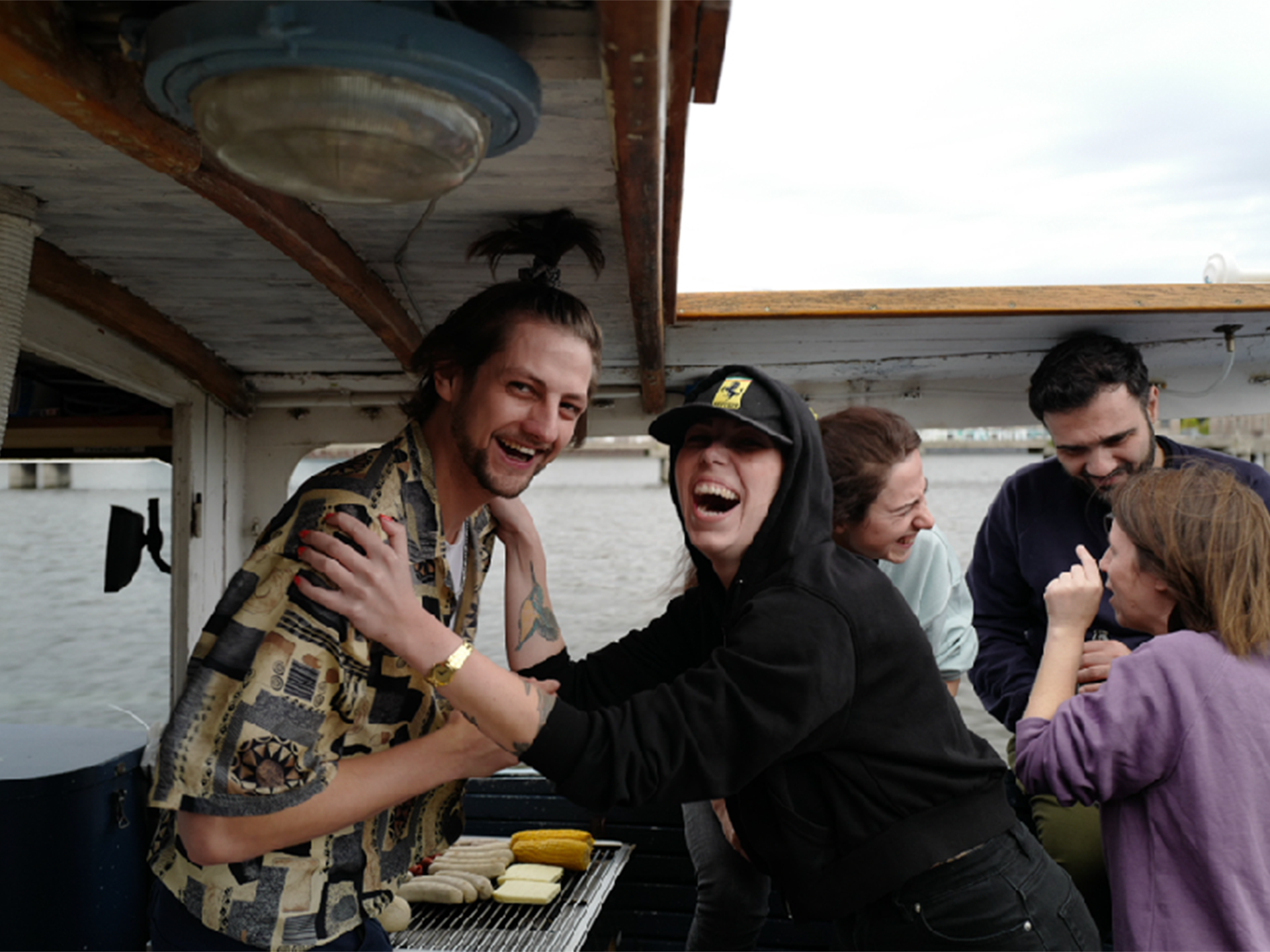 Image of two laughing, goofing employees of Jung von Matt SPREE on a boat. In the background other employees.