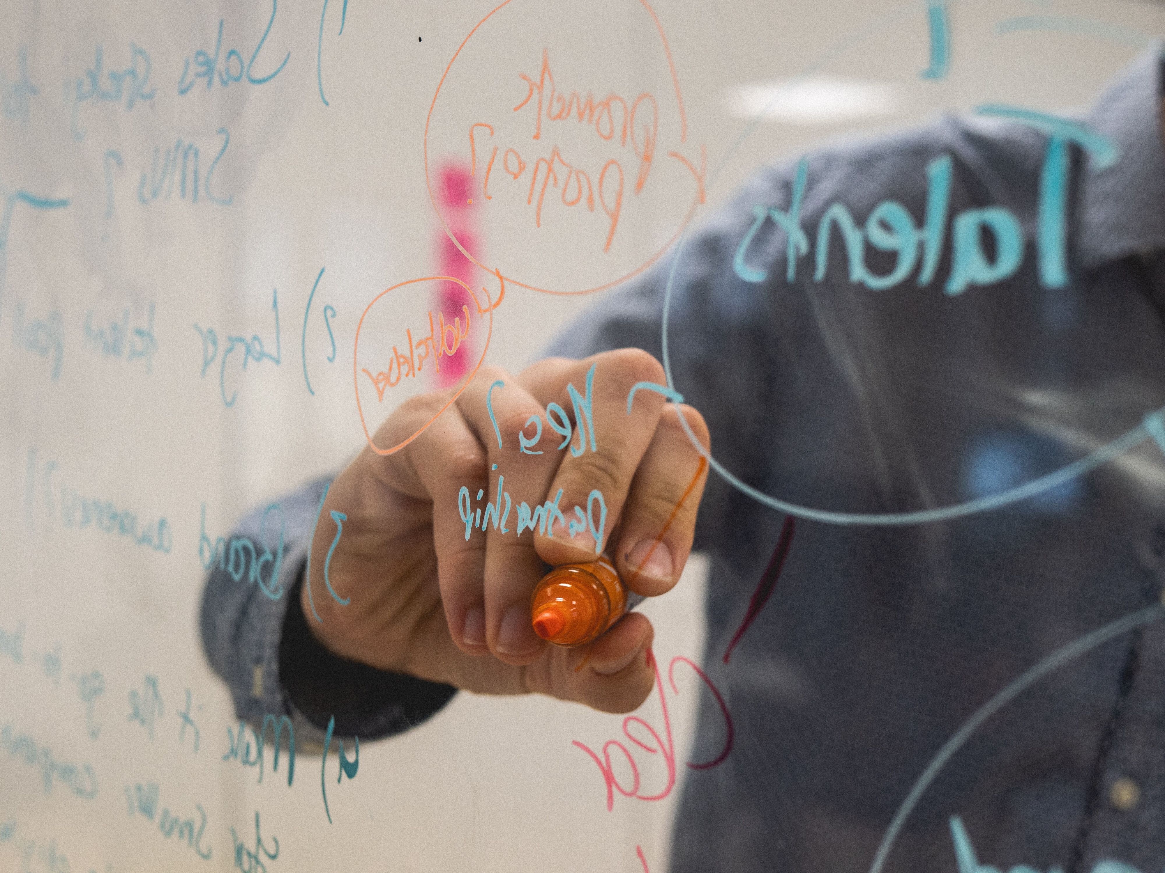 Image of a hand of a man from Morrow in blue shirt making notes on a transparent board with an orange pen.